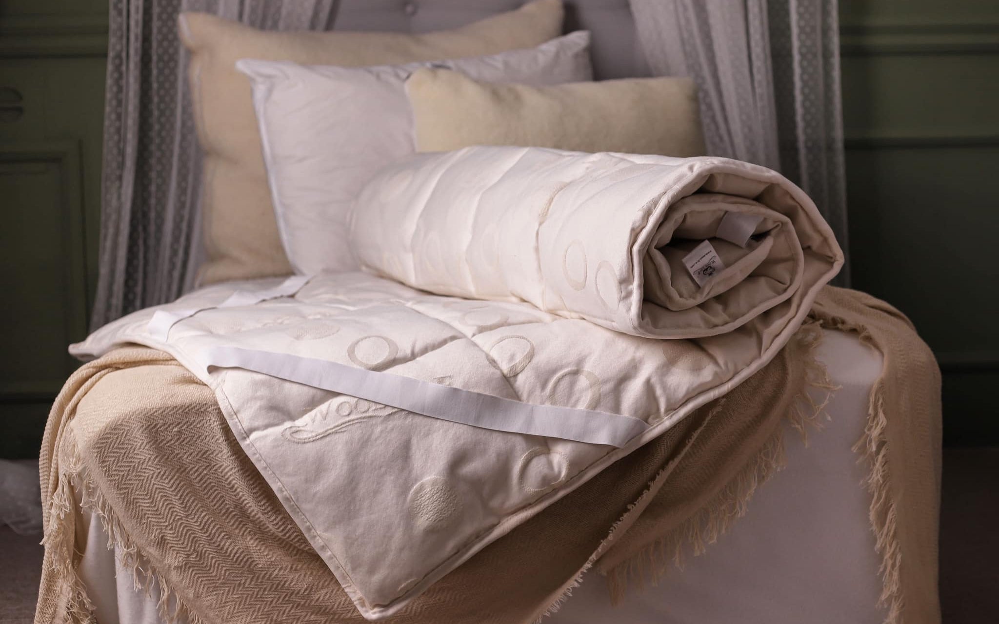 Das Wool-Line Unterbett Schurwolle Lux liegt eingerollt auf einem Bett. Das Futter aus Schurwolle ist 100% natürlich und von handverlesenen Schäfern bezogen und zeigt hier seine ganze Elastizität.