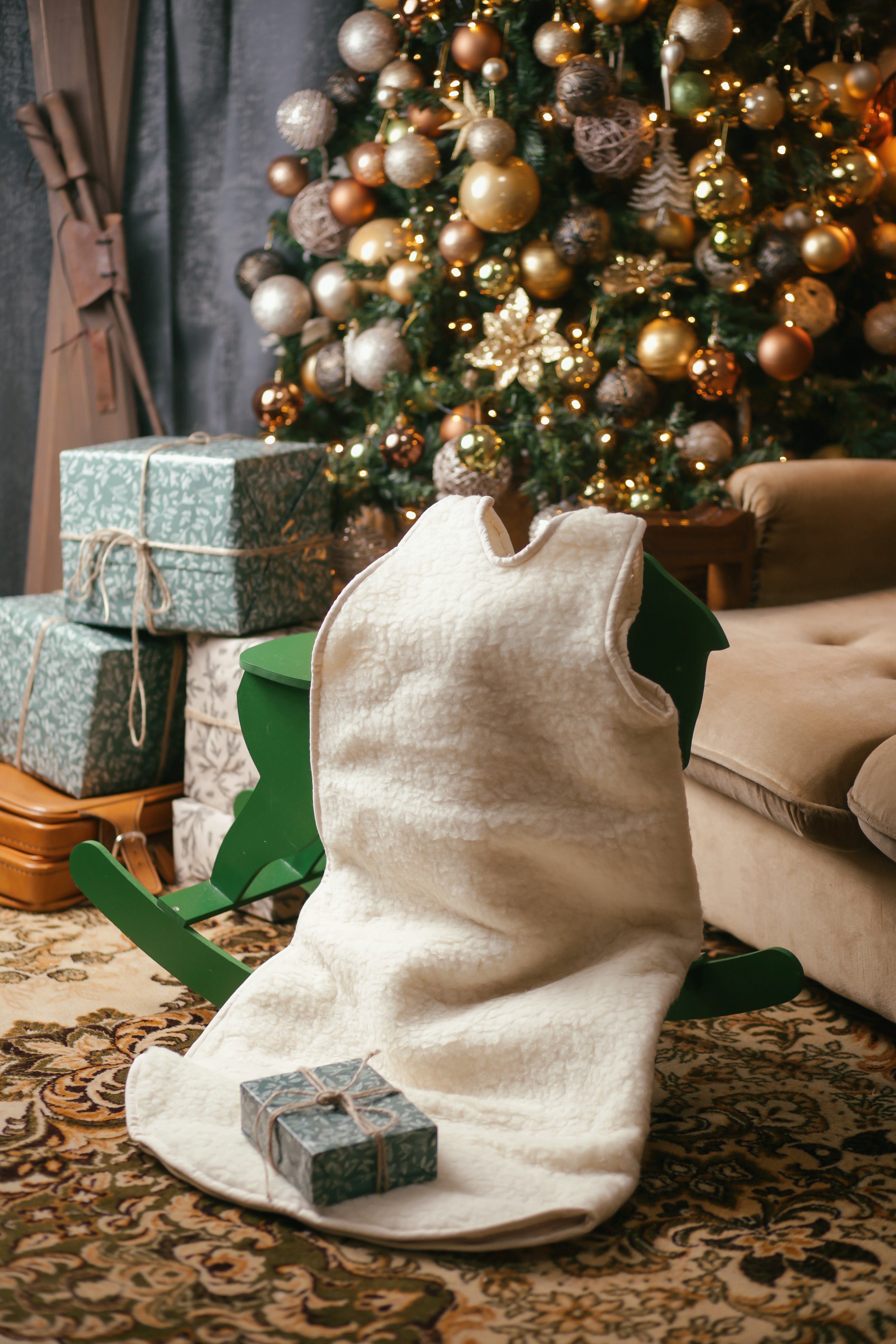 Der Babyschlafsack von Wool-Line eignet sich perfekt für den Winter. Hier ist er vor einem mit goldenen Kugeln geschmückten Weihnachtsbaum ausgestellt. Der beige Babyschlafsack ist aus weicher und natürlicher Schafschurwolle hergestellt. Im Hintergrund sind vier Päckchen als Geschenke zu sehen.