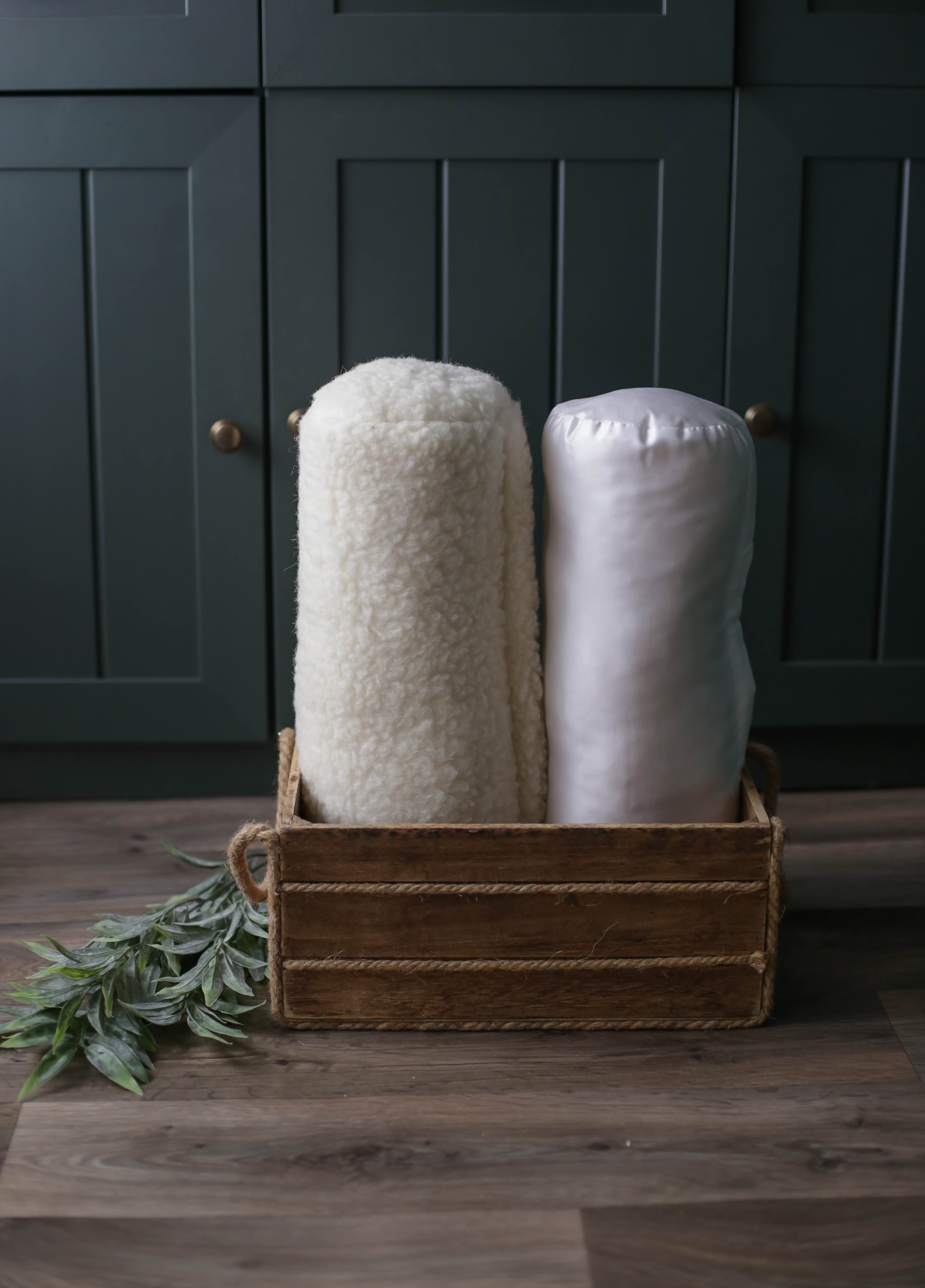 Die Bio-Nackenrolle weiß mit Bio-Baumwollbezug ist gemeinsam mit unserem Gold-Modell mit Filzbezug in einer dekorativen Holzkiste aufgestellt.
