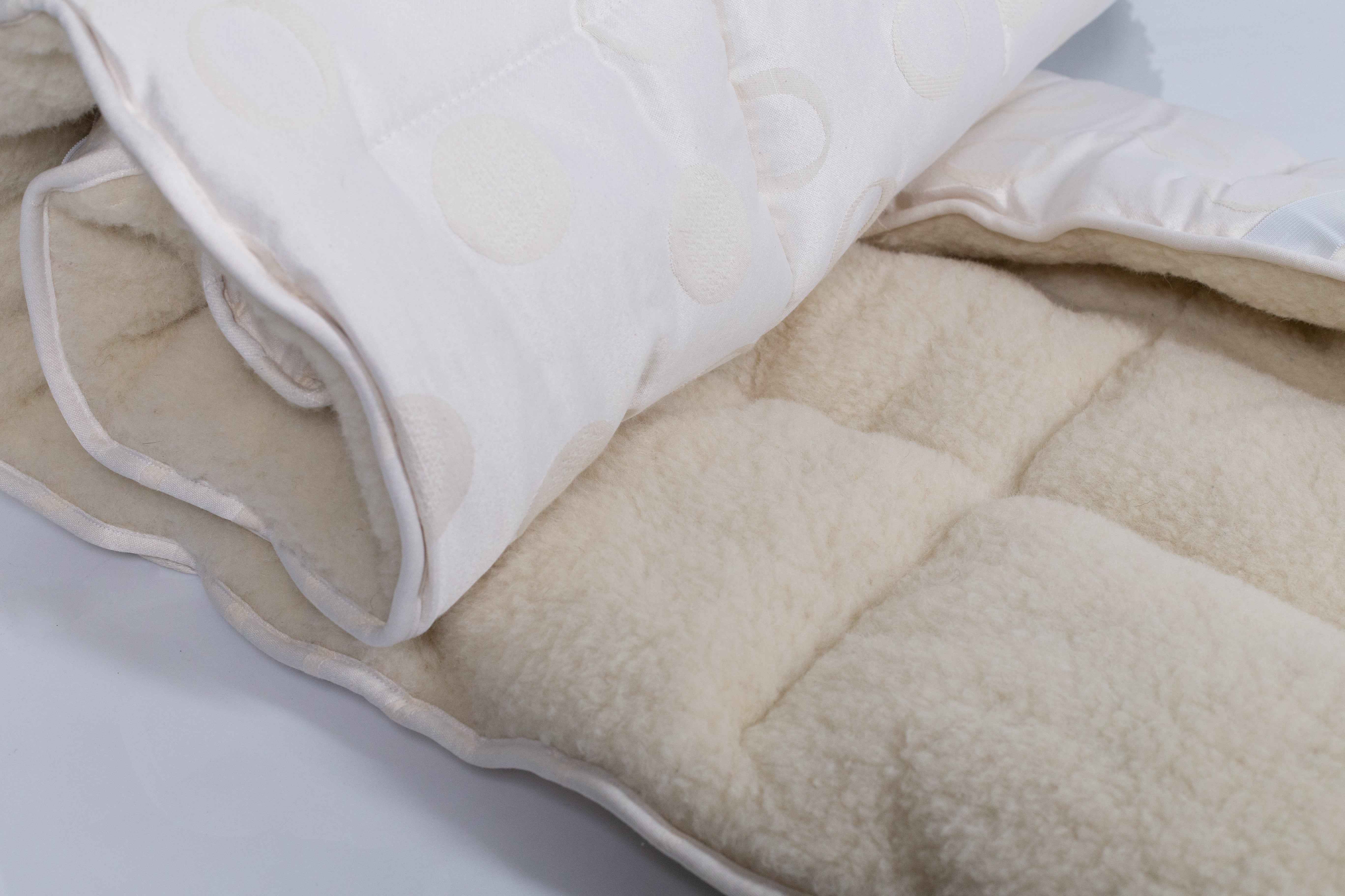 Der Bio-Matratzentopper Gold/Lux auf weißem Untergrund. Er ist teilweise zusammengelegt und eingerollt, und zeigt damit seine gesamte Elastizität.