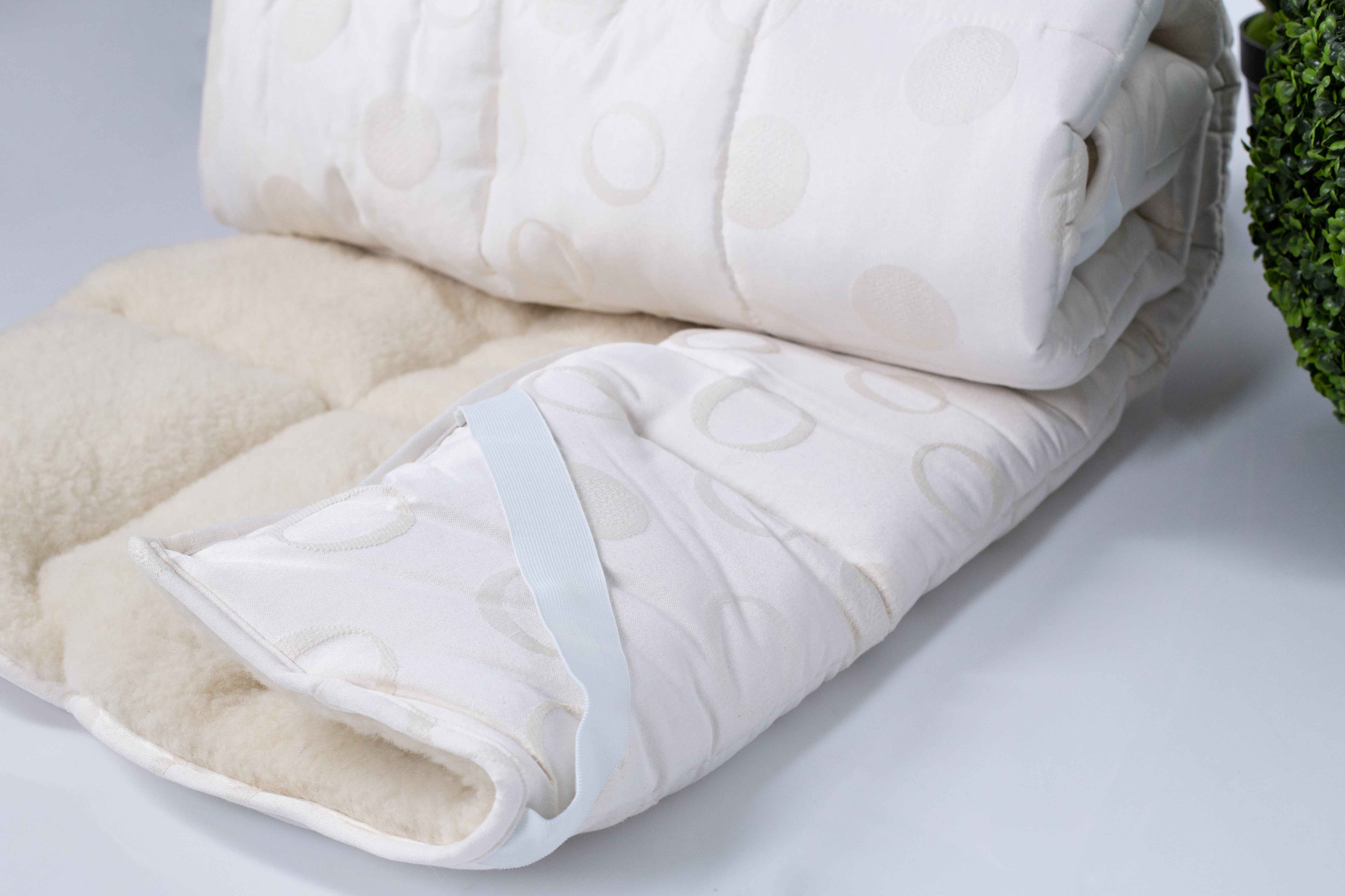 Der Bio-Matratzen Topper aus Schurwolle Gold Lux eingerollt und teilweise zusammengelegt aus weißem Untergrund.