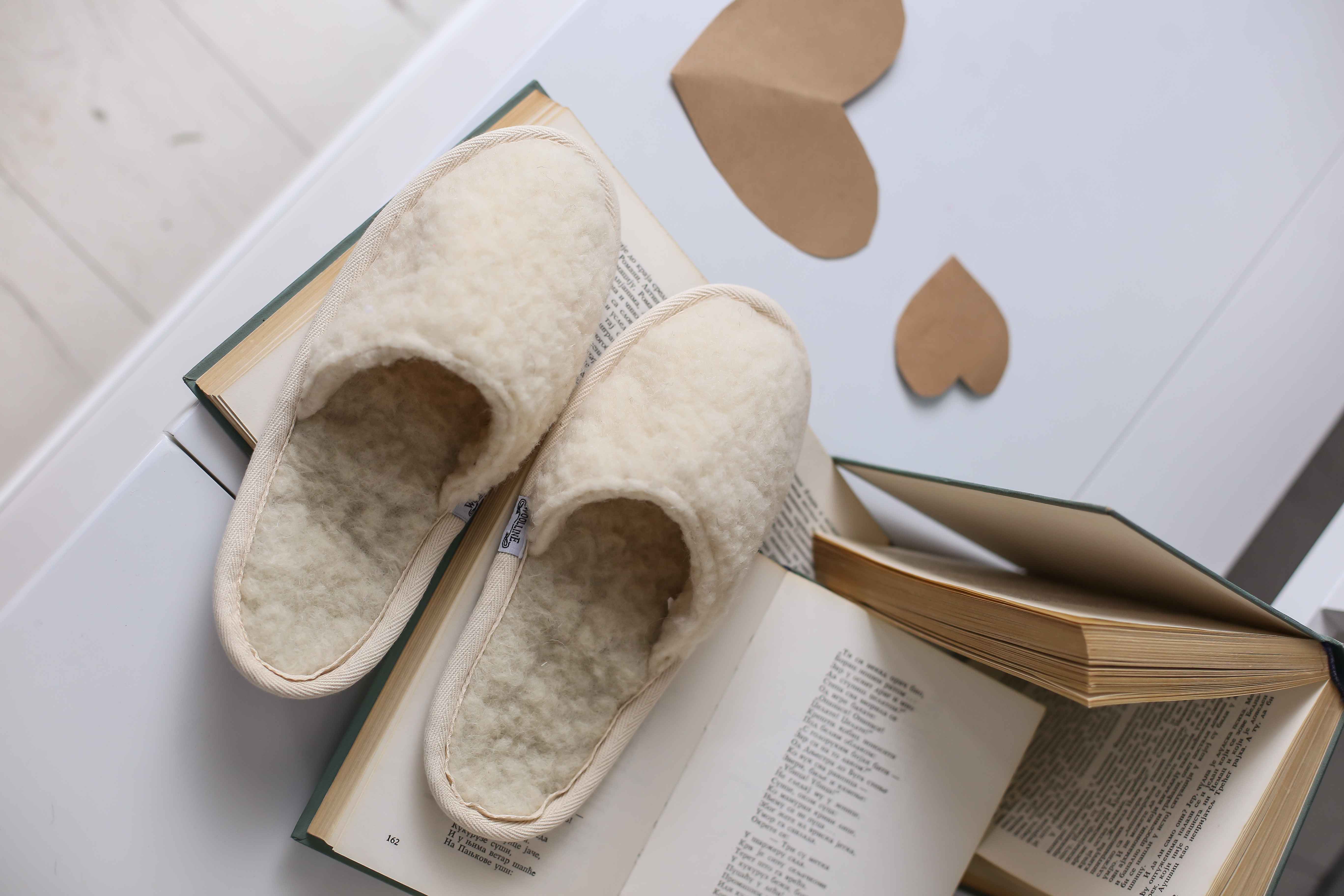 Die Filzpantoffeln aus reiner Schafschurwolle zwischen drei Büchern abgestellt. Das Futter und der Bezug aus weichem Filz ist in der Nahaufnahme in seinen Konturen gut zu sehen. Über den Filzpantoffeln sind zwei kleinen Papierherzen zur Dekoration abgelegt.