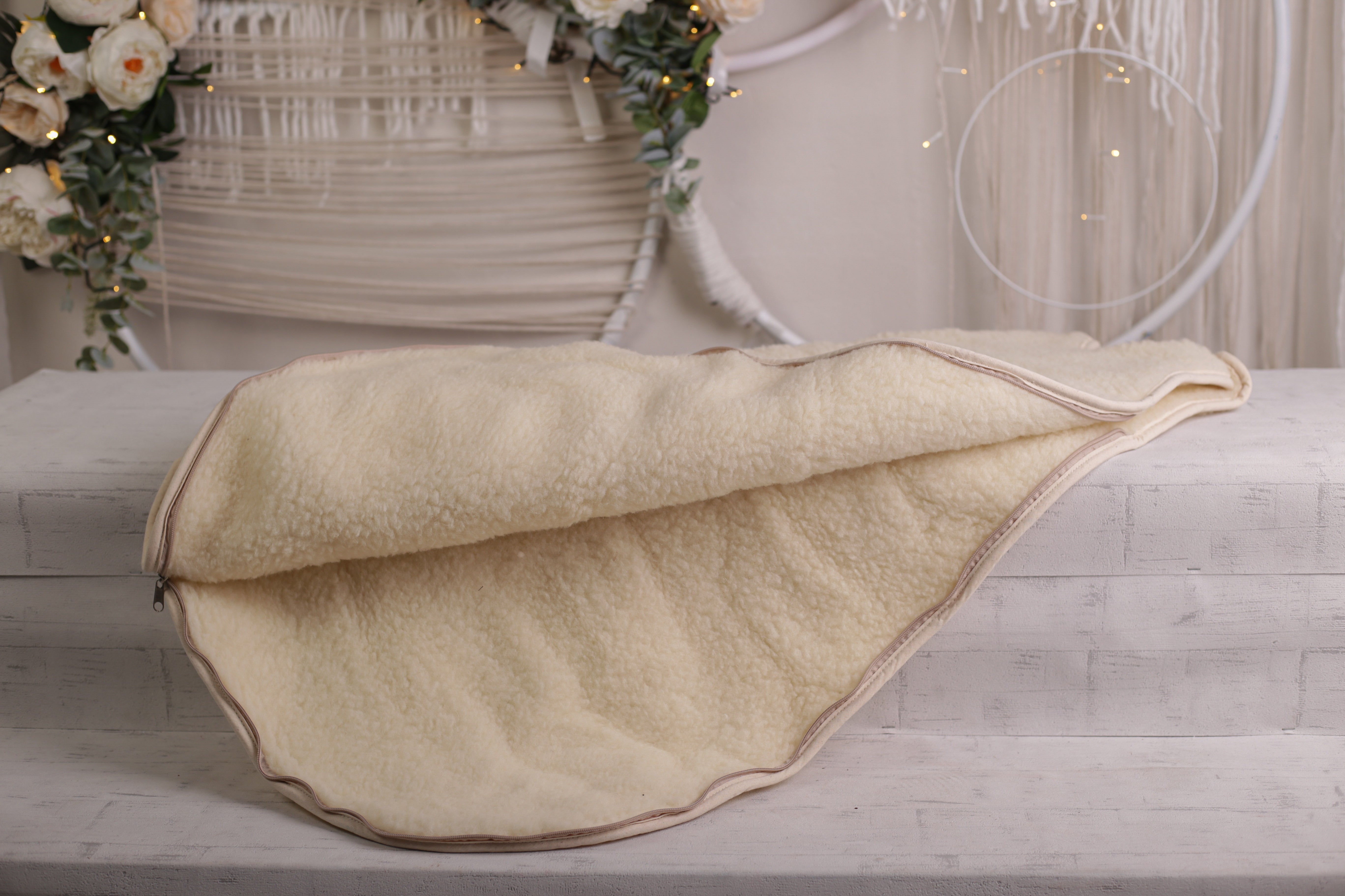 Der Ganzjahres Babyschlafsack von Wool-Line auf einer weißen Ablage. Der Reißverschluss ist geöffnet und bietet einen Blick in das Innenfutter aus feinem Schurwollfilz, das im Winter wärmt und im Sommer angenehm kühlt.