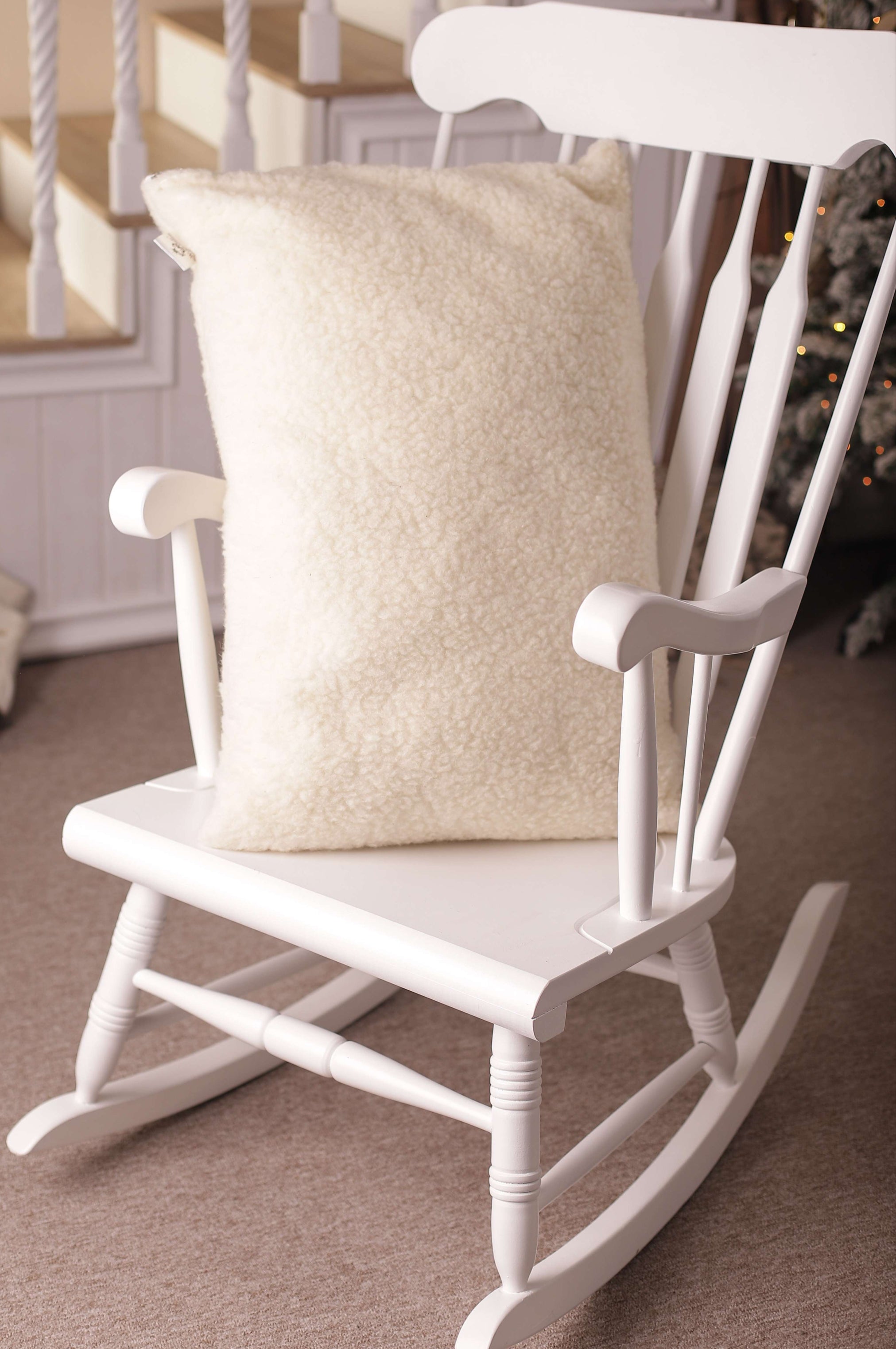 Das Kissen mit Schafschurwolle Gold ist auf einen weißen Schaukelstuhl gestellt. Der weiche Bezug aus biologischem Filz ist in seinen Konturen gut zu sehen.