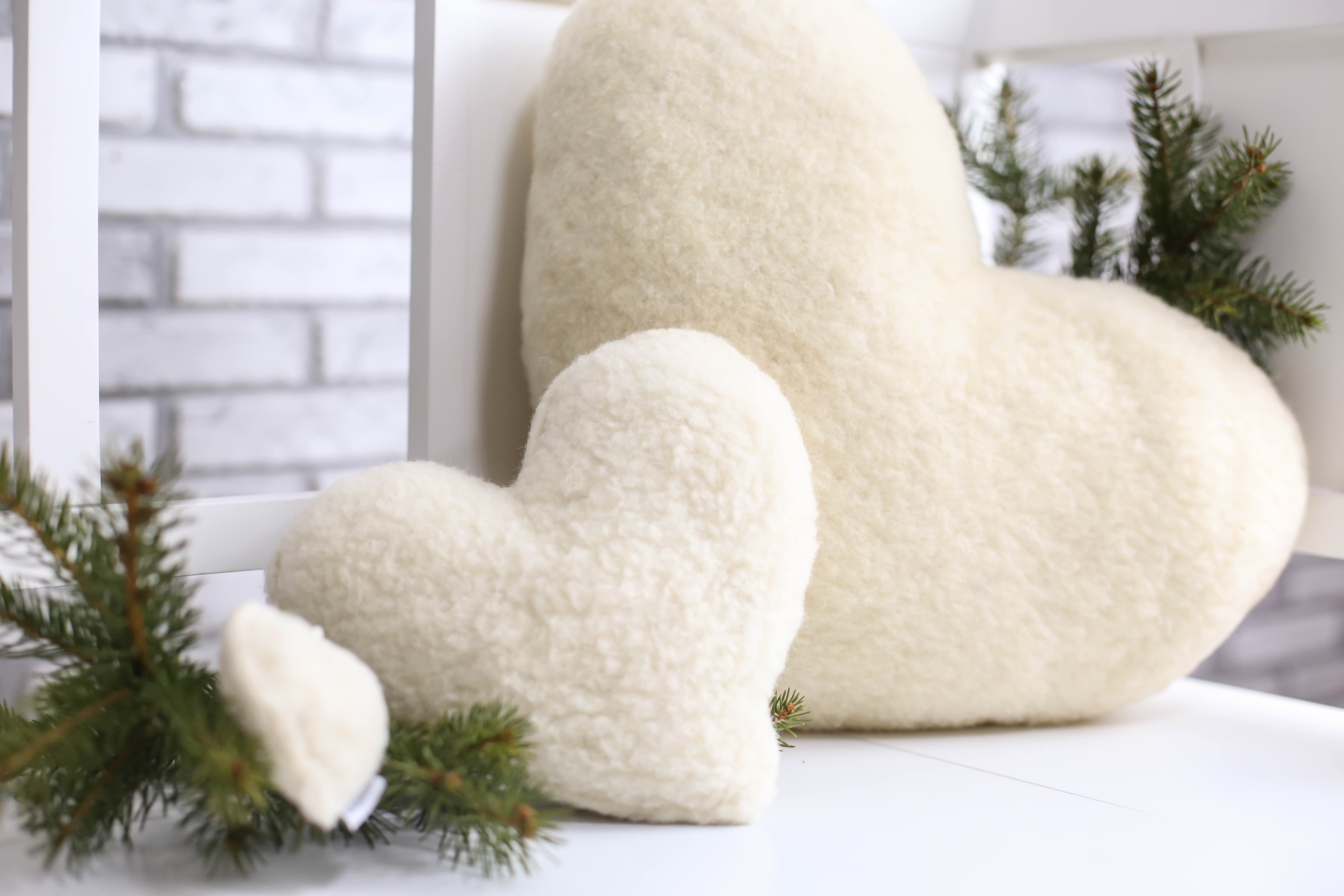 Drei Kissen in Herzform, ein kleines, ein mittelgroßes und ein großes Kissen nacheinander aufgereiht auf einer weißen Gartenbank.