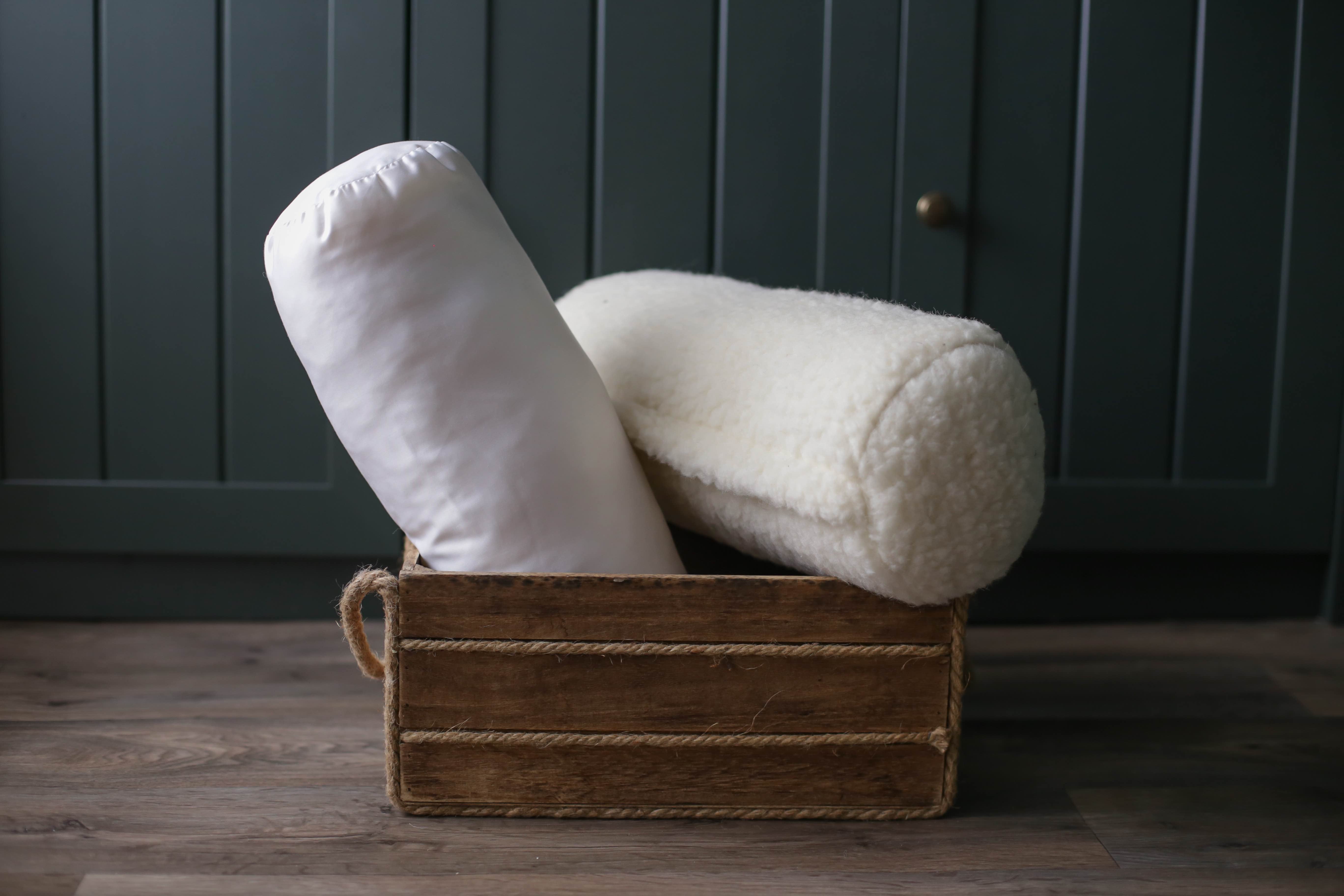 Die Wool-Line Knierolle Lux und die Nackenrolle Gold liegen gemeinsam in einer kleinen Holzkiste.