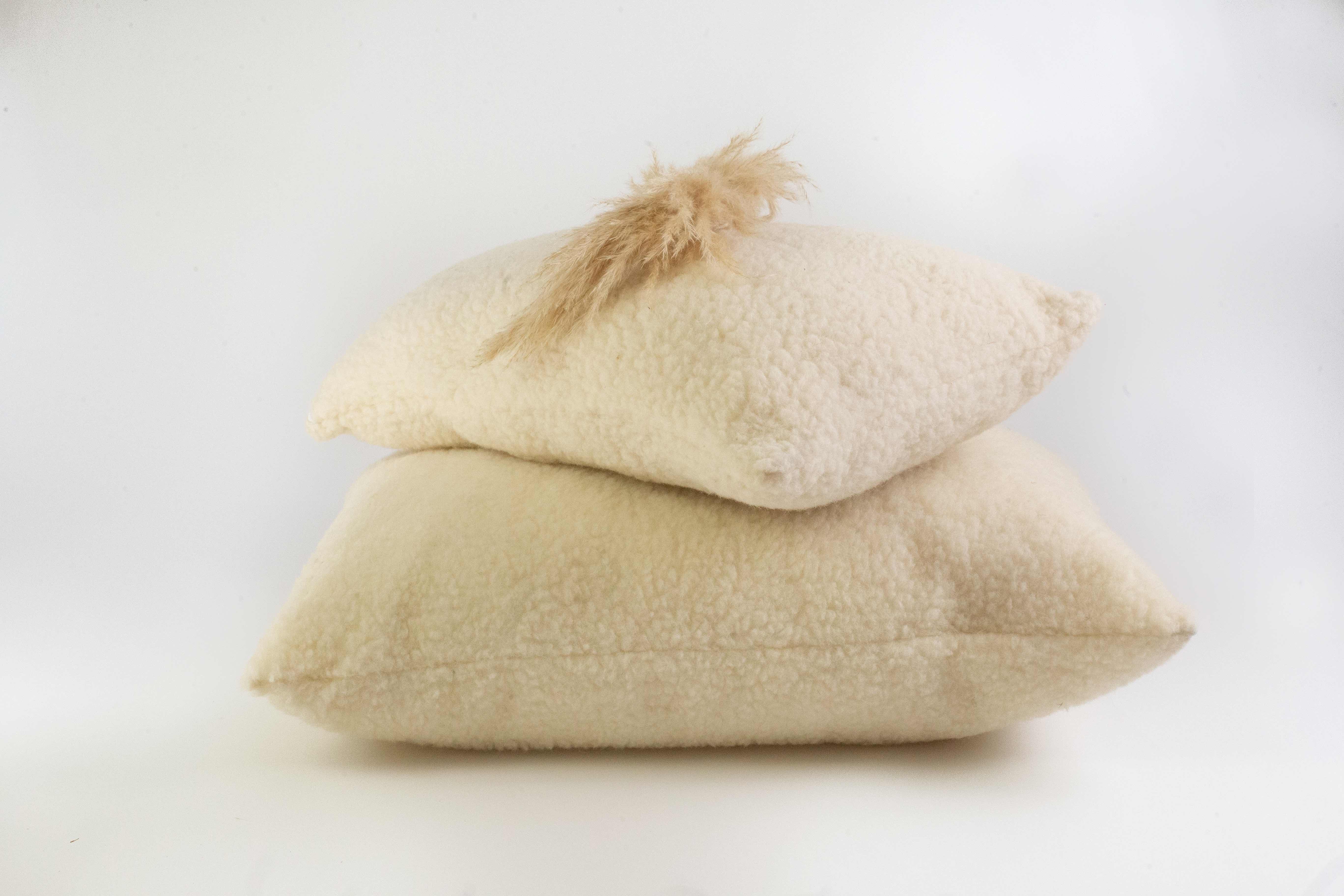 Zwei Kopfkissen aus Schafschurwolle Gold von Wool-Line aufeinandergestapelt auf weißem Untergrund. An der Spitze schaut ein Teil der biologischen Schafschurwoll-Füllung heraus, die flexibel entnommen oder aufgefüllt werden kann.