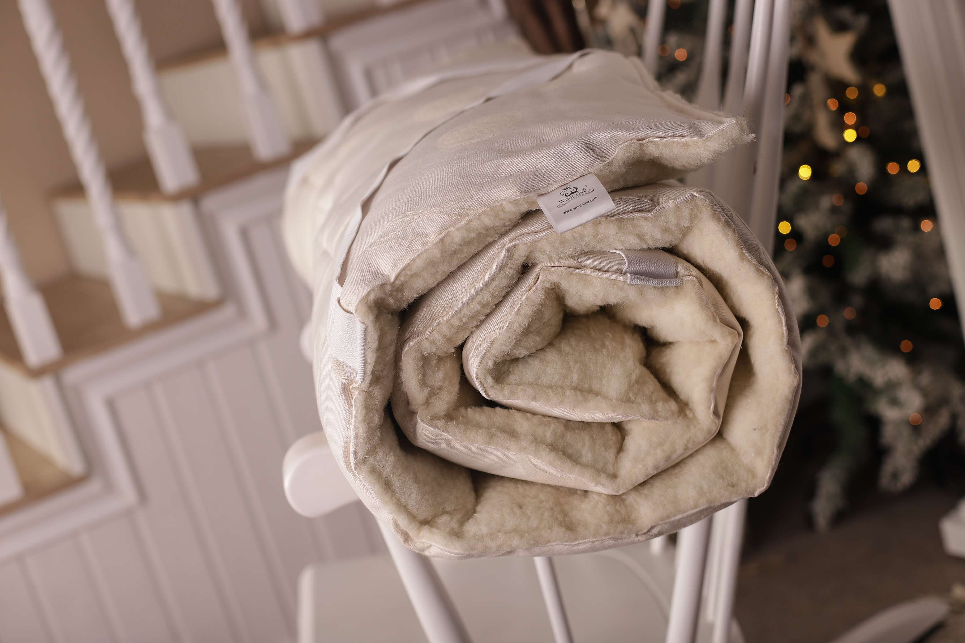 Der Matratzentopper Natur Gold/Lux eingerollt auf einem weißen Schaukelstuhl.