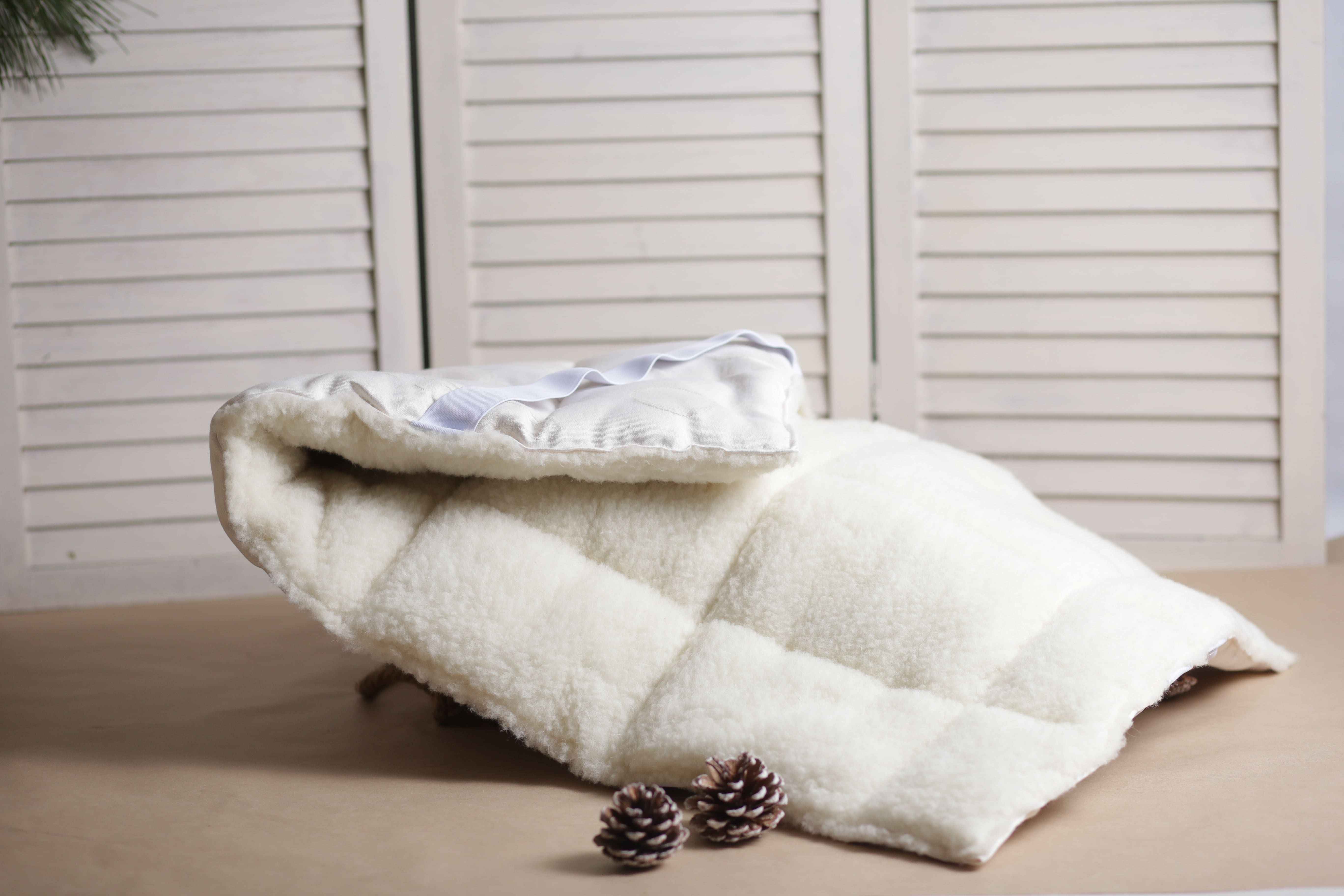 Unser Matratzentopper Bio Gold/Lux von Wool-Line liegt zusammengelegt auf einer kleinen Anhöhe. Davor sind zwei dekorative Tannenzapfen zu sehen, was die Natürlichkeit des Toppers widerspiegeln soll.