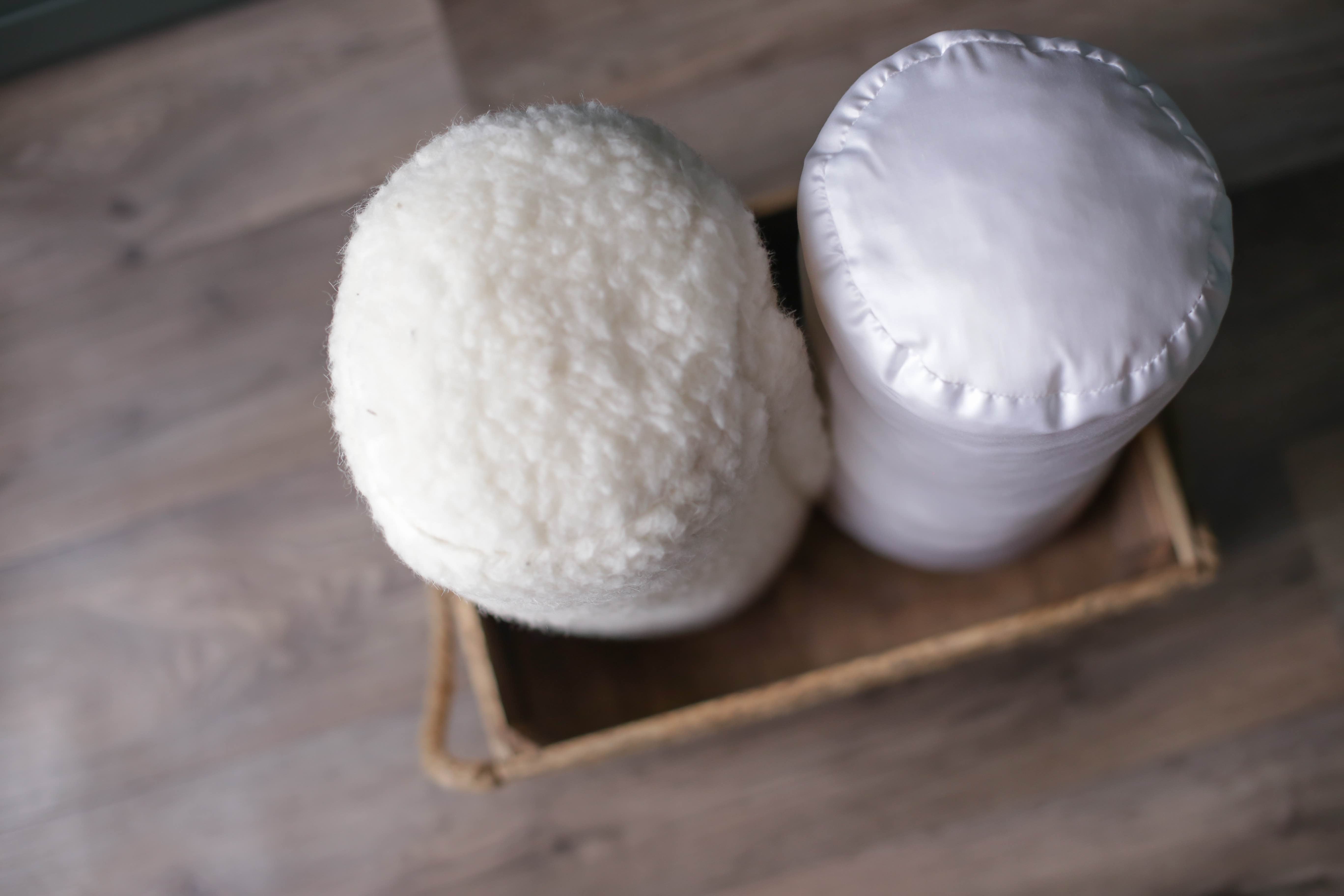 Unsere beinen Nackenkissen, beziehungsweise Nackenrollen nebeneinander in einer dunkelbraunen Holzkiste aufgestellt. Rechts befindet sich die Nackenrolle wei´ß mit Bio-Baumwollbezug, die auch als Knierolle verwendet werden kann. Links ist die Nackenrolle beige Gold zu sehen.