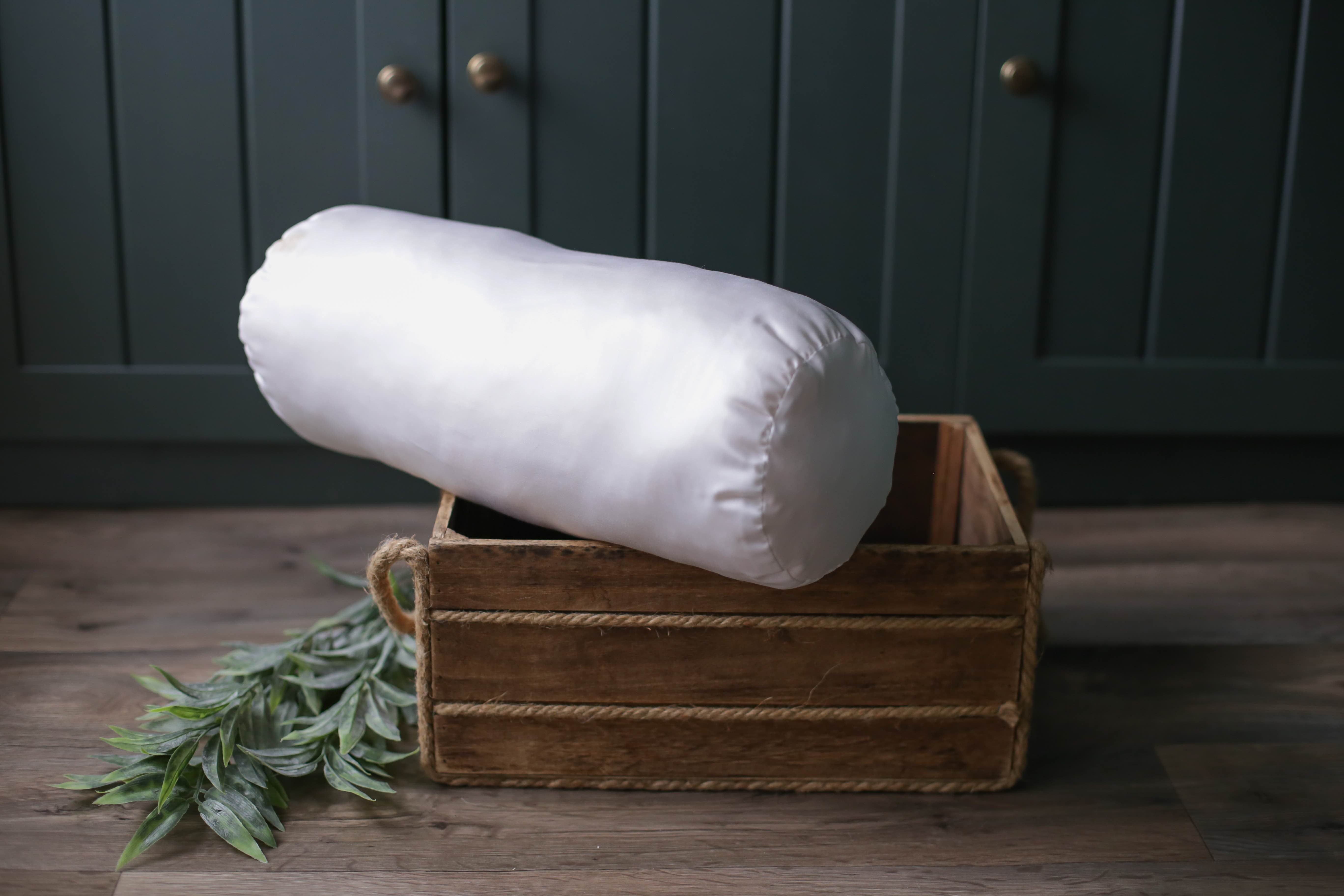 Die Nackenrolle Bio von Wool-Line auf einer kleinen dunkelbraunen Holzkiste ausgestellt. Die Nackenrolle ist mit dem Bezug aus Bio-Baumwolle bezogen und mit echter Schafschurwolle gefüllt.