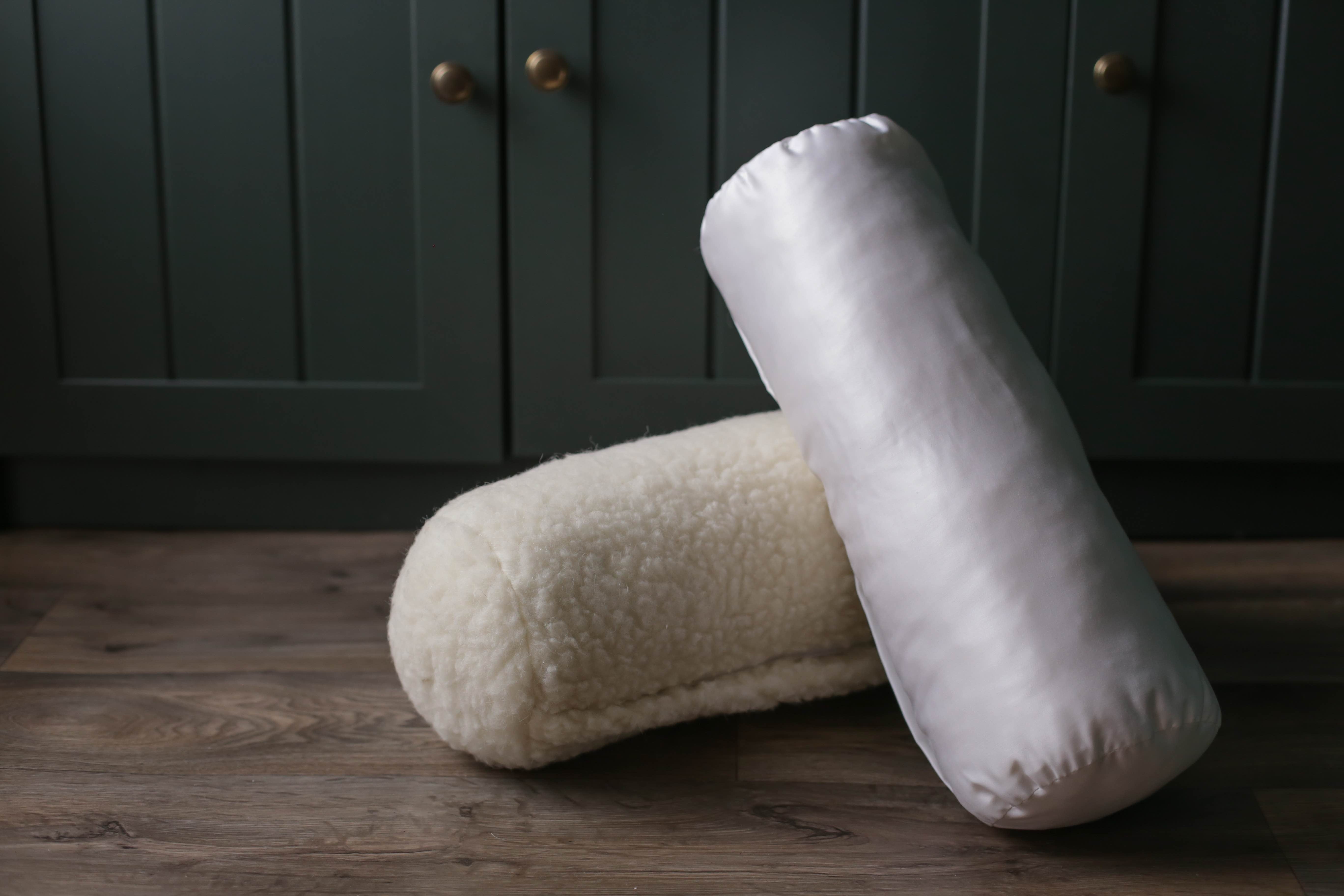 Zwei Nackenrollen aus Schafwolle von Wool-Line aufeinandergestapelt. Die Nackenrolle mit Baumwollbezug lehnt direkt auf der Nackenrolle Gold aus 100% Schafschurwolle.