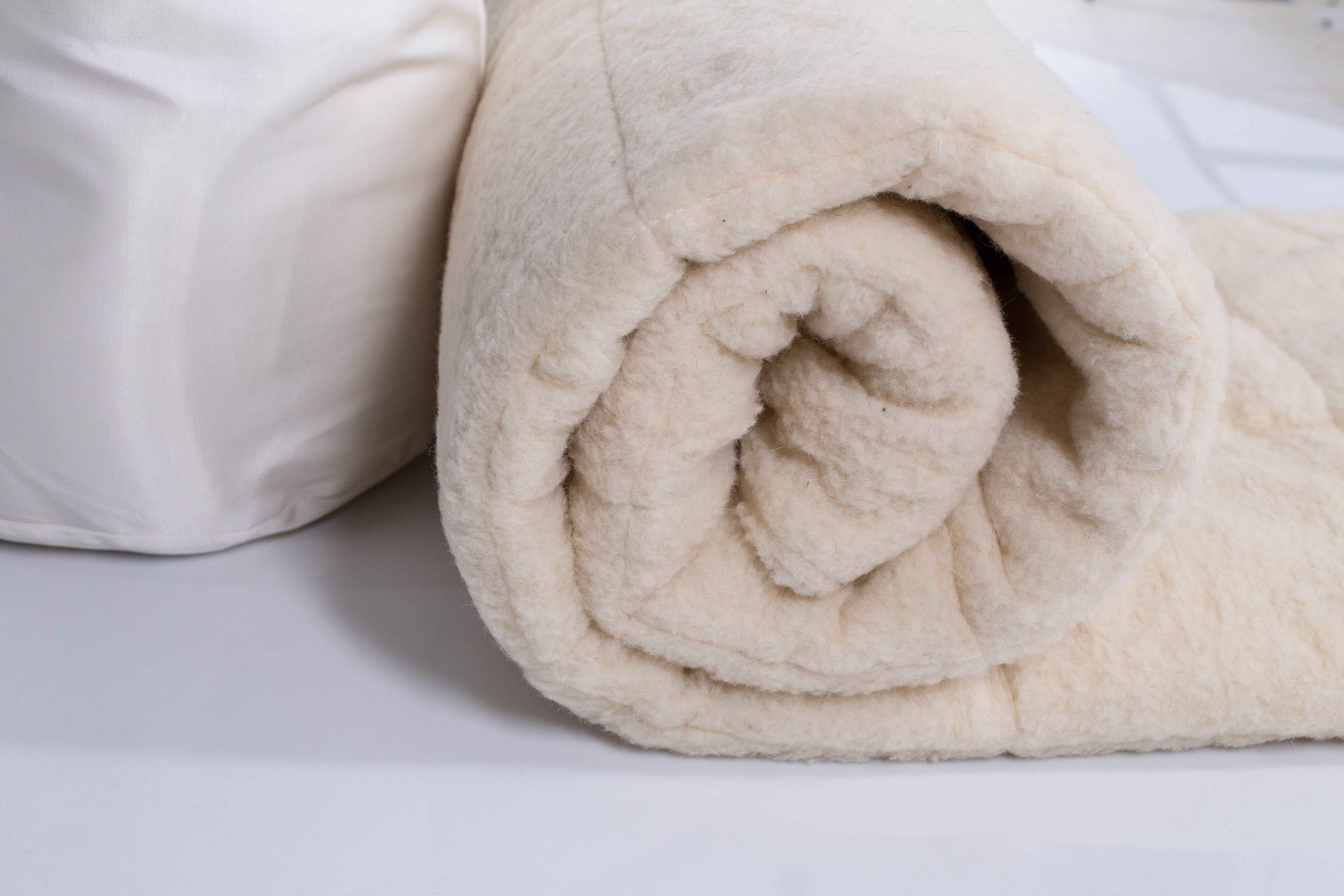 Die Bettdecke Schafschurwolle Gold von Wool Line eingerollt auf dem Bett. Der feine und weiche Filzbezug ist detailliert in einer Nahaufnahme zu sehen.