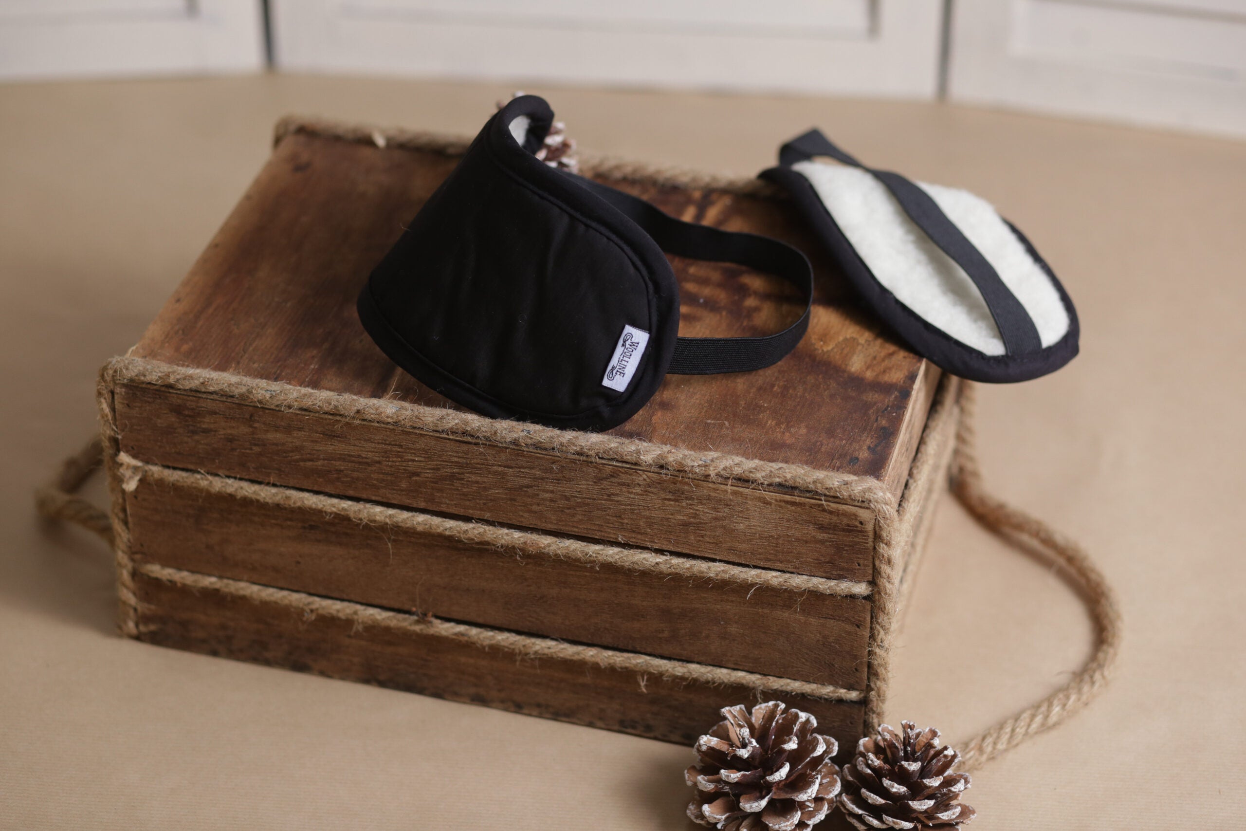 Zwei Schlafmaske Bio auf einer kleinen Ablage aus dunkelbraunem Holz. Links ist die Außenfläche aus Bio-Baumwolle zu sehen, während der feine natürliche Wollfilz aus Schafschurwolle auf der anderen Seite zum Vorschein kommt.