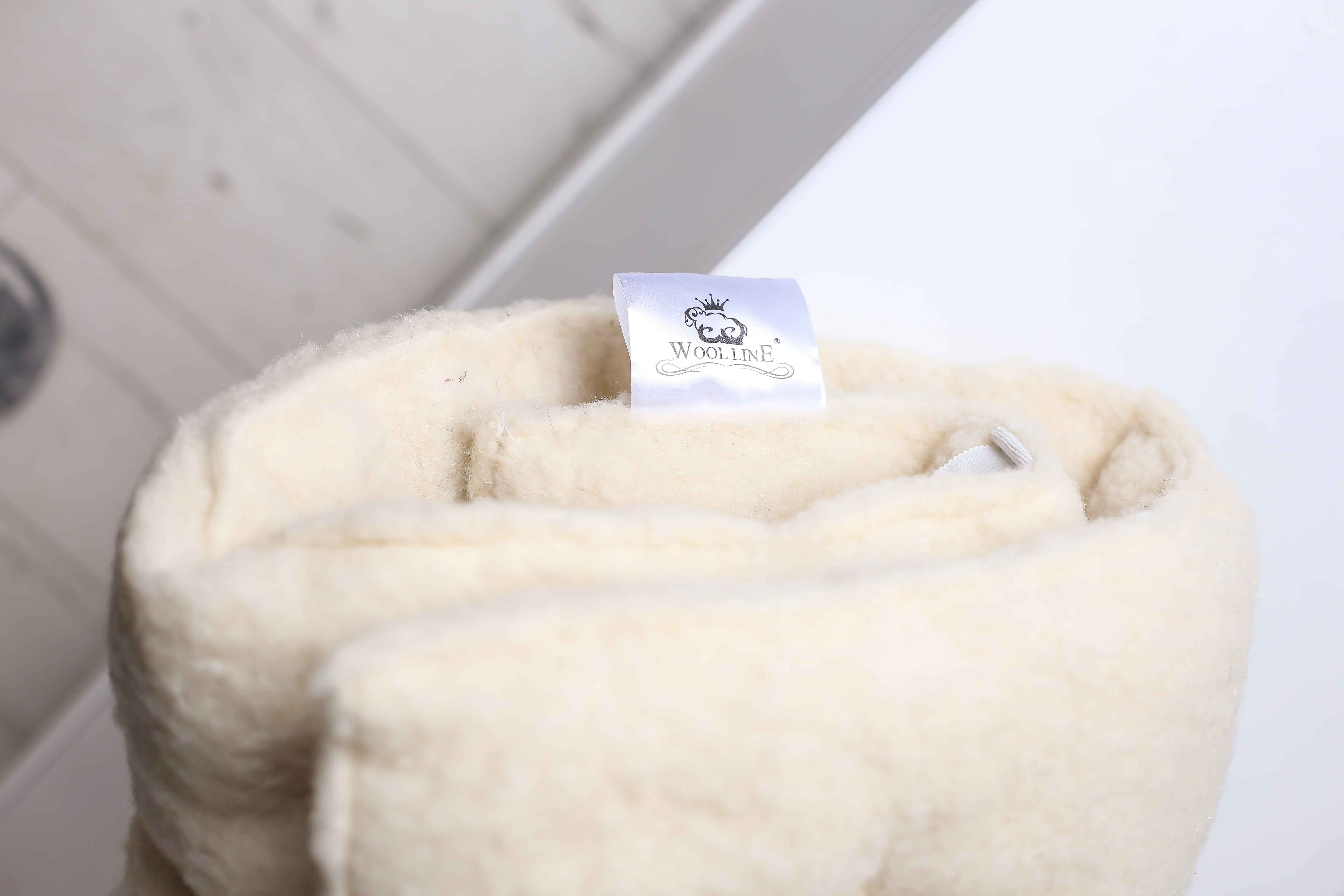 Die Oberseite einer eingerollten Schurwolle Matratzenauflage von Wool-Line. Ganz oben ist ein kleiner Zettel mit dem Wool-Line Logo zu sehen.