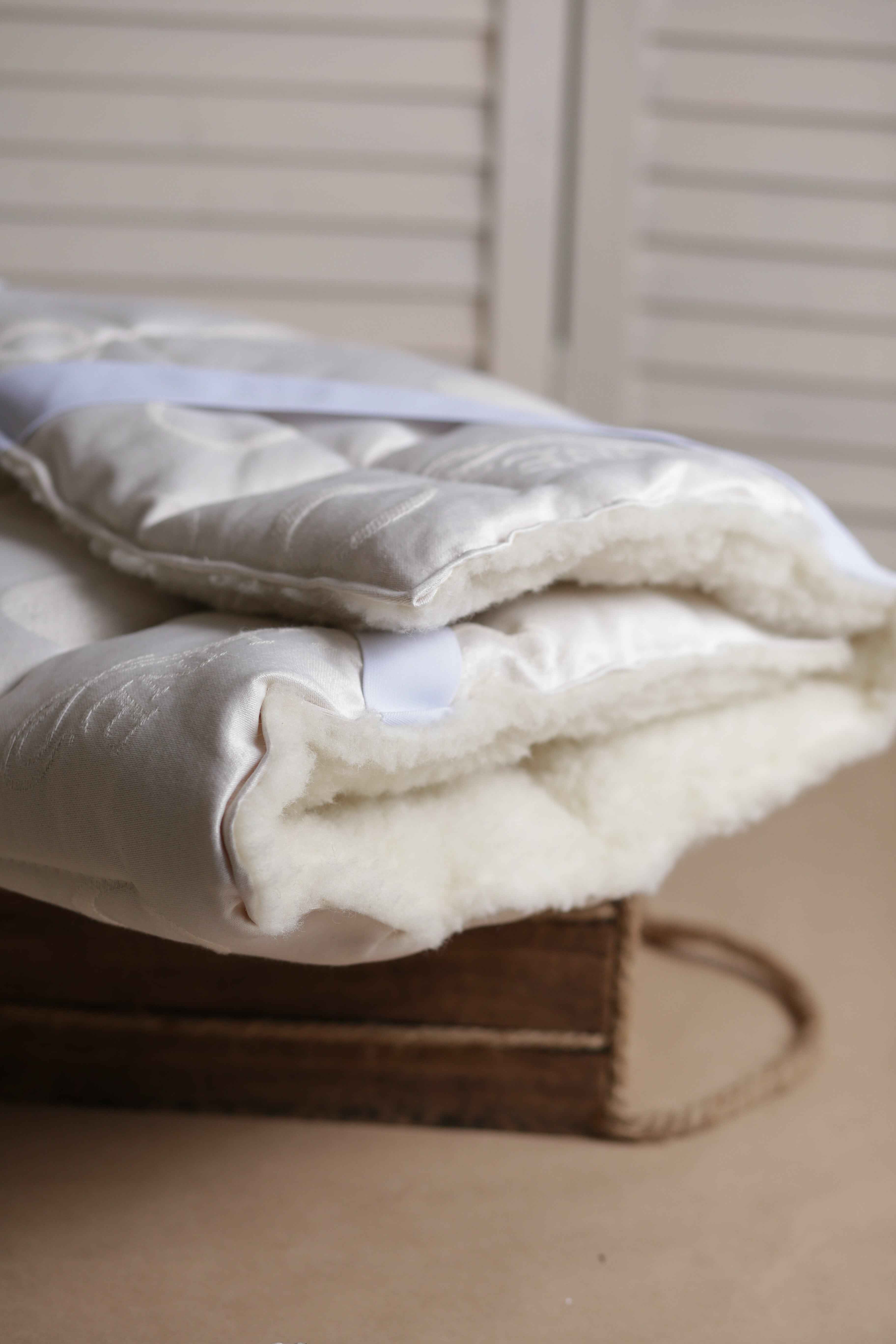 Der Topper Natur Gold Lux von Wool-Line liegt auf einer kleinen Anhöhe aus dunkelbraunem Holz. An der Seite sind feine Filzkonturen zu sehen.