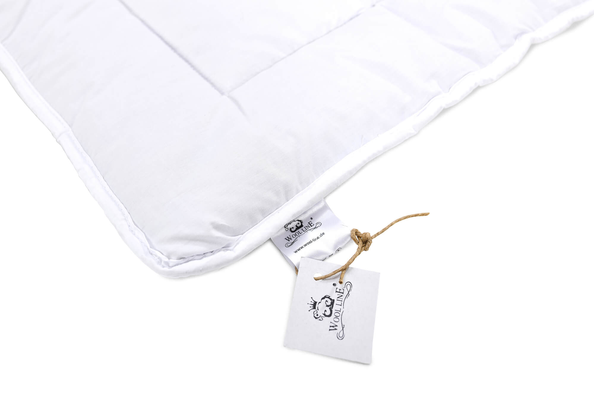 Die Wickelauflage für Babys von Wool-Line auf weißem Untergrund fotografiert. Der Fokus liegt auf einem an der Schurwolle-Wickelauflage angebrachten kleinen Zettel, auf dem das Wool-Line Logo abgedruckt ist.
