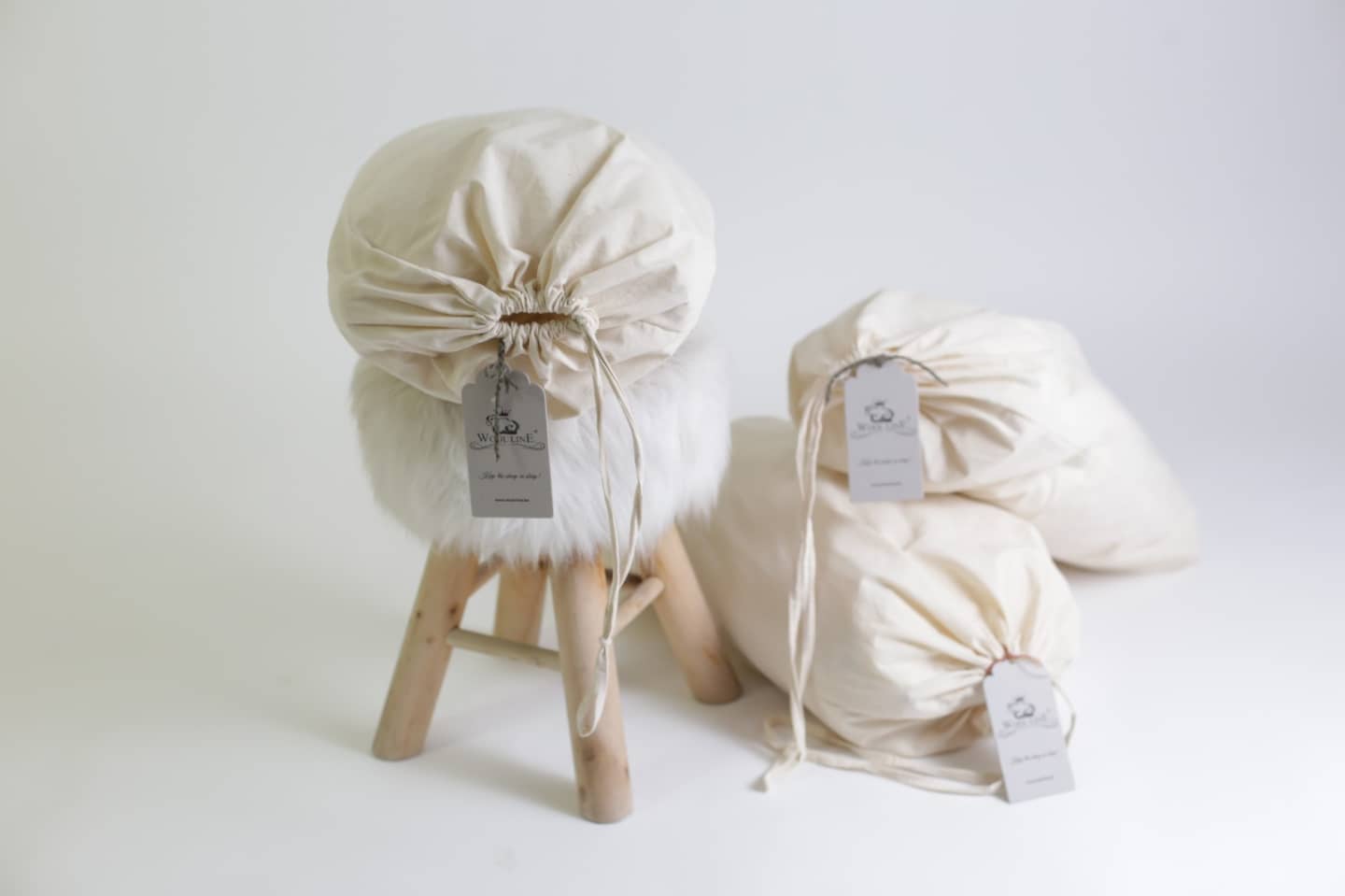 Drei Bettdecken Lux von Wool-Line in Beutel aus Bio-Baumwolle verpackt und bereit zum Kundenversand. Die Lieferungen von Wool-Line erfolgen alle komplett plastikfrei. An der Spitze der Verpackungen befinden sich kleine Zettel, auf denen das Wool-Line-Logo zu sehen ist. 