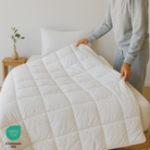 Eine weiße Bettdecke aus reiner Schurwolle Lux von Wool-Line wird sanft und flach auf das Bett gelegt.