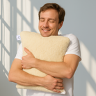 Ein junger Mann presst das Wool-Line Gold-Kissen aus Schafschurwolle ganz eng gegen die Brust. Sein Gesichtsausdruck ist entspannt. 