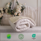 Die Schurwolle Bettdecke Gold Lux auf einer schönen Ablage. Die Decke ist eingerollt und zeigt seine natürliche Elastizität. Im unteren Teil befinden sich Bio-Siegel und das Siegel OEKO TEX Standard 100, was zeigt, dass alle Materialien nachhaltig, sicher und ohne Chemikalien sind. 