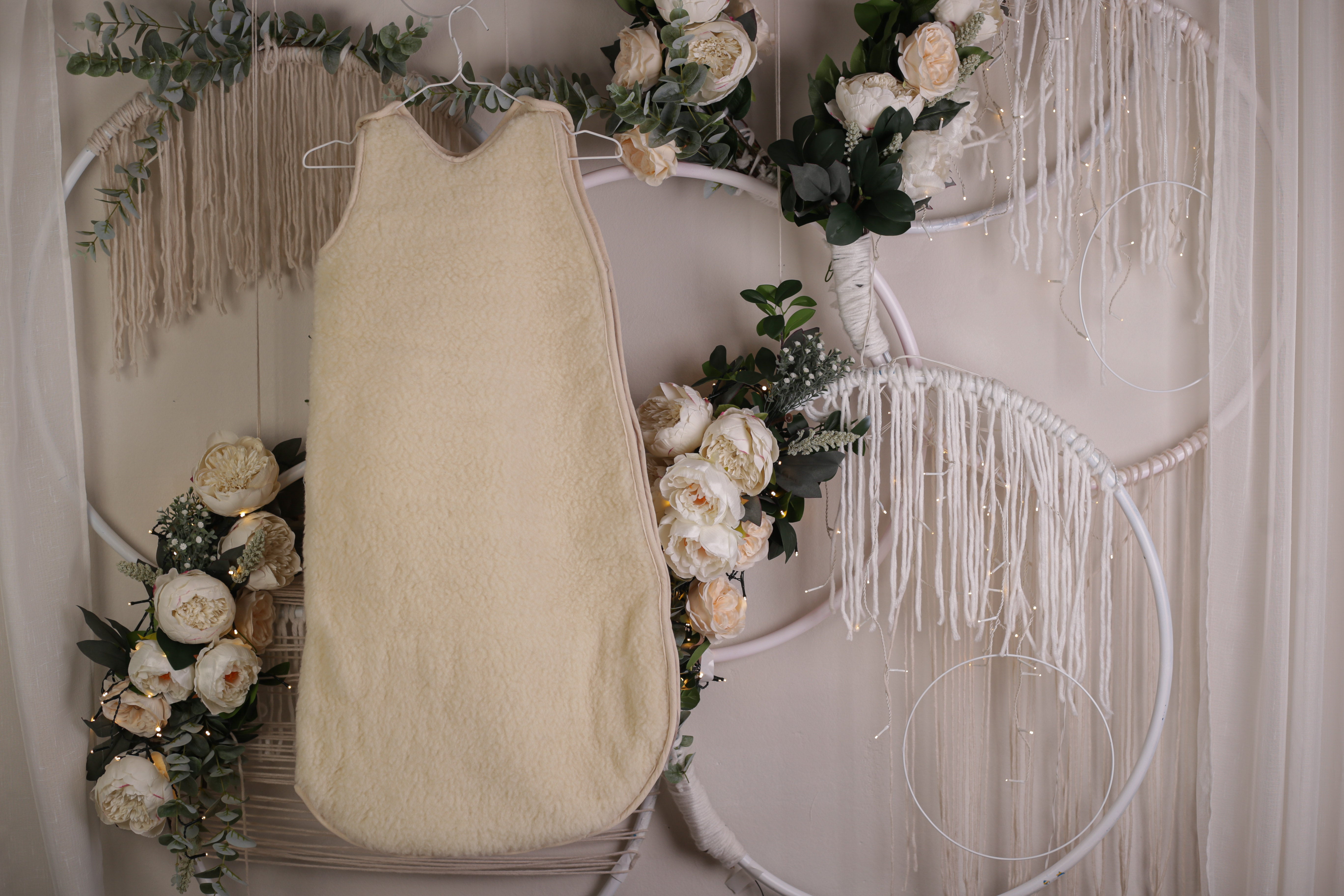 Der Babyschlafsack zum Mitwachsen von Wool-Line aufgehängt auf einem Kleiderbügel. Im Hintergrund befinden sich mit weißen Rosen dekorierte Traumfänger. 