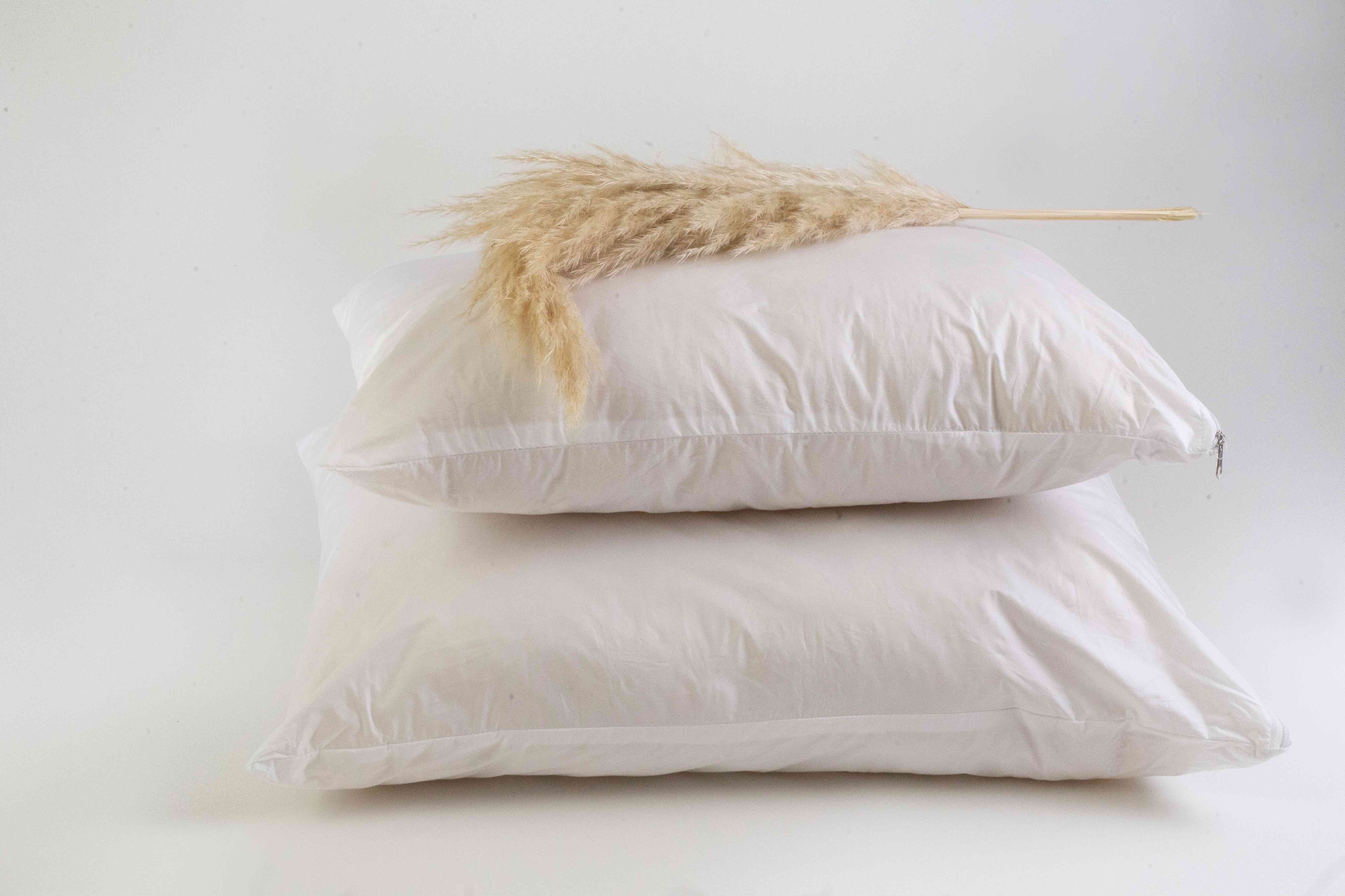 Zwei Kissen Schurwolle Lux-Modelle aufeinandergestapelt auf weißem Untergrund. An der Spitze des oberen Kissen befindet sich eine dekorative Äre. 