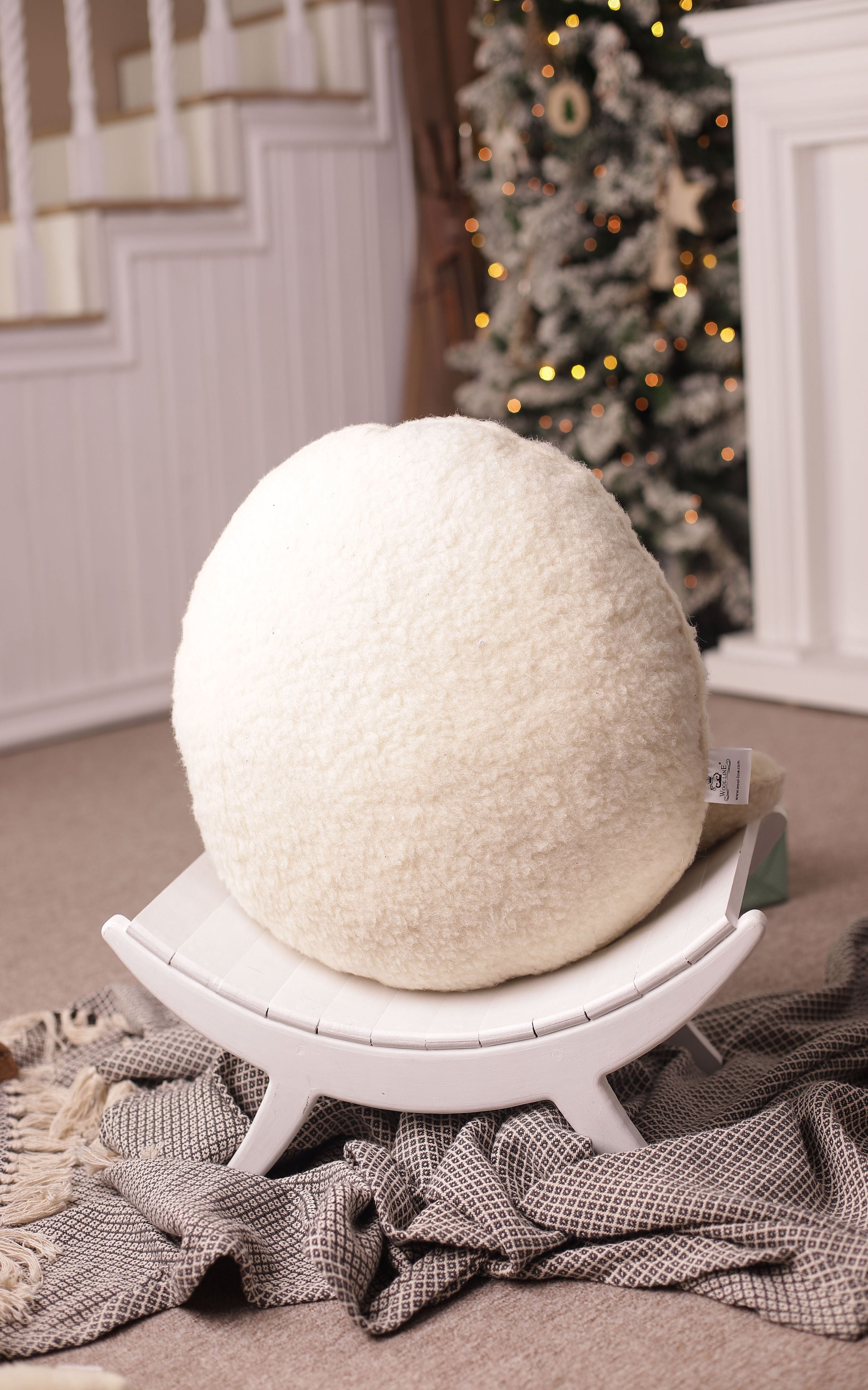 Das Kissen beige rund von Wool-Line auf einer gebogenen weißen Holzablage abgestellt. Die weichen Filzkonturen sind selbst von der Ferne gut zu erkennen. 