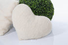 Das weiße Kuschelherz Kissen von Wool-Line auf weißem Untergrund fotografiert. Im Hintergrund befindet sich eine runde, güne Pflanze. Der weiche Filz des Herzkissens ist detailliert und gut ausgeleuchtet zu sehen. 