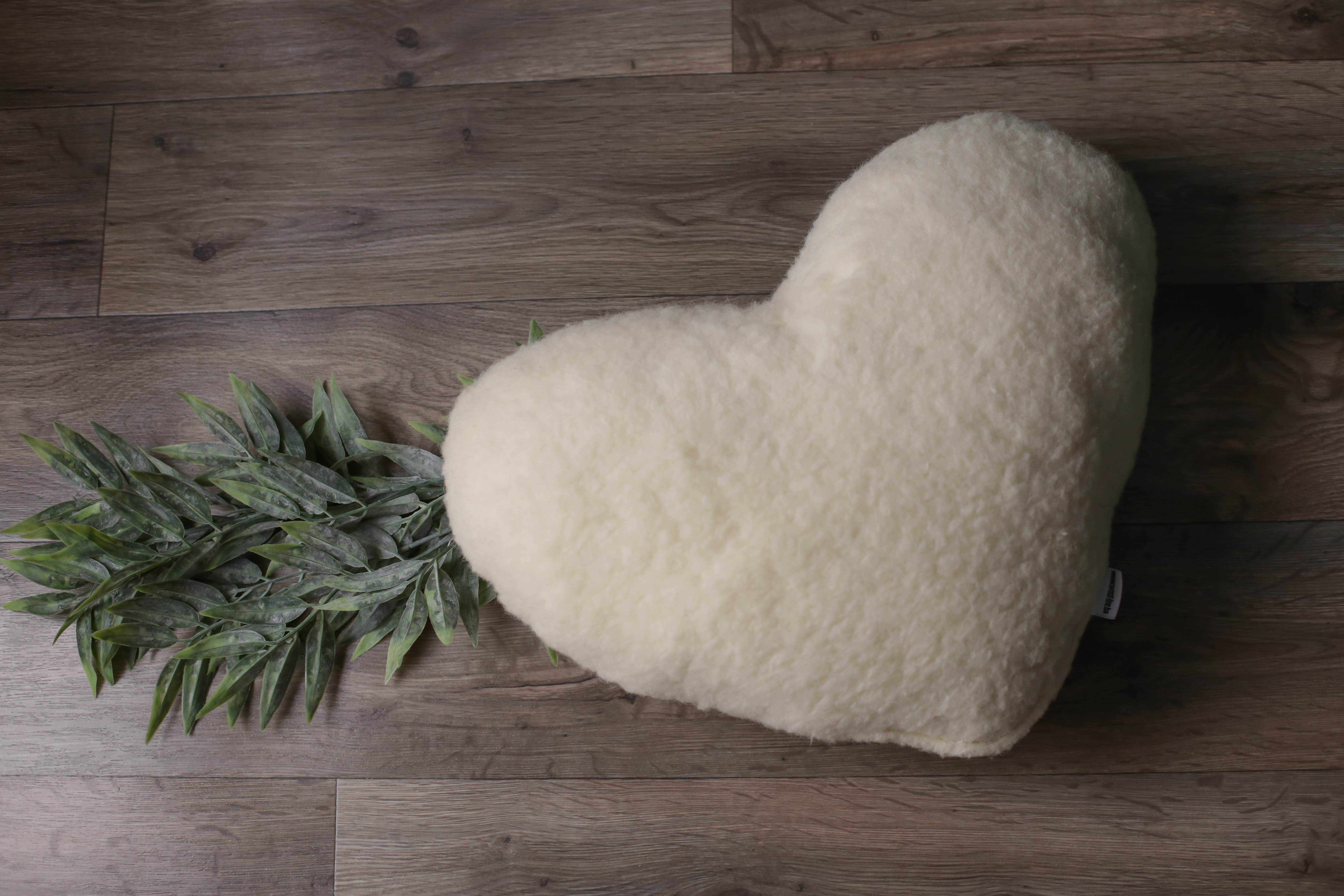 Eine kleinere Version unseres Kuschelherzkissen von Wool-Line auf einem dunkelbraunen Holzfußboden abgelegt. 