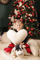 Das Kuschelkissen Herz von Wool-Line in den Händen eines glücklich lächelnden Mädchen, das zirka 10 Jahre alt ist. Im Hintergrund steht ein Weihnachtsbaum geschmückt mit roten, weißen und goldenen Kugeln. Das Mädchen hat das Herzkissen offenbar zu Weihnachten geschenkt bekommen. 