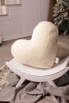 Das Kuschelkissen in Herzform von Wool-Line auf einem kleinen weißen Hocker aufgestellt. Unter der Anhöhe befindet sich eine kleine schwarz-weiß-karierte Decke. 