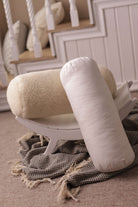 Unsere beinen Nackenrollen/ Nackenkissen auf einem Bild. Im Vordergrund befindet sich das mit Bio-Baumwolle bezogene Lux-Modell, auf einer kleinen Holzablage ist die Nackenrolle beige Gold von Wool-Line zu sehen. 