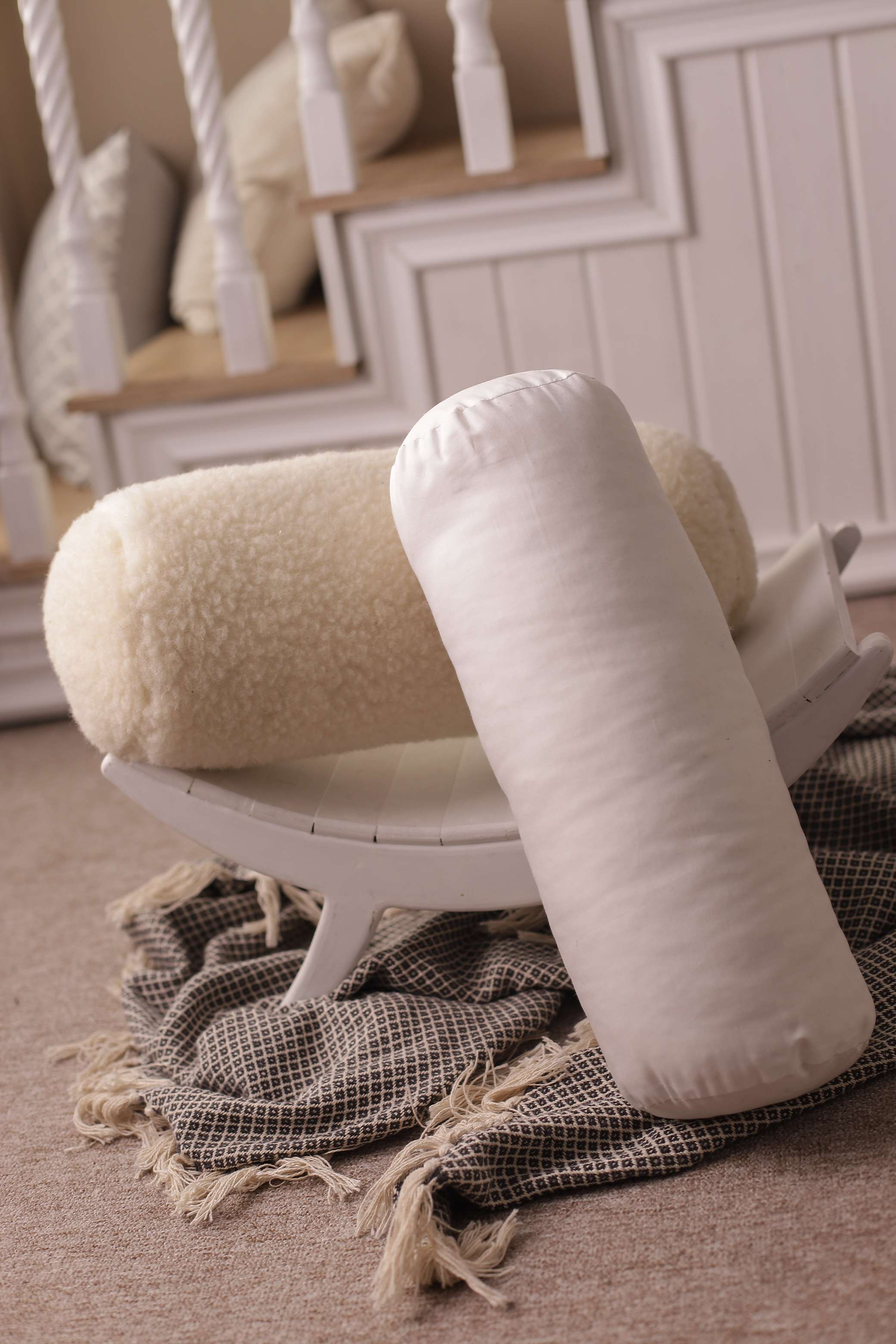 Die beiden Nackenrollen von Wool-Line auf einem Bild. Auf einer kleinen weißen Ablage liegt die Nackenrolle beige Gold, während die weiße Nackenrolle mit Bio-Baumwollbezug an dem anderen Nackenkissen angelehnt ist. 