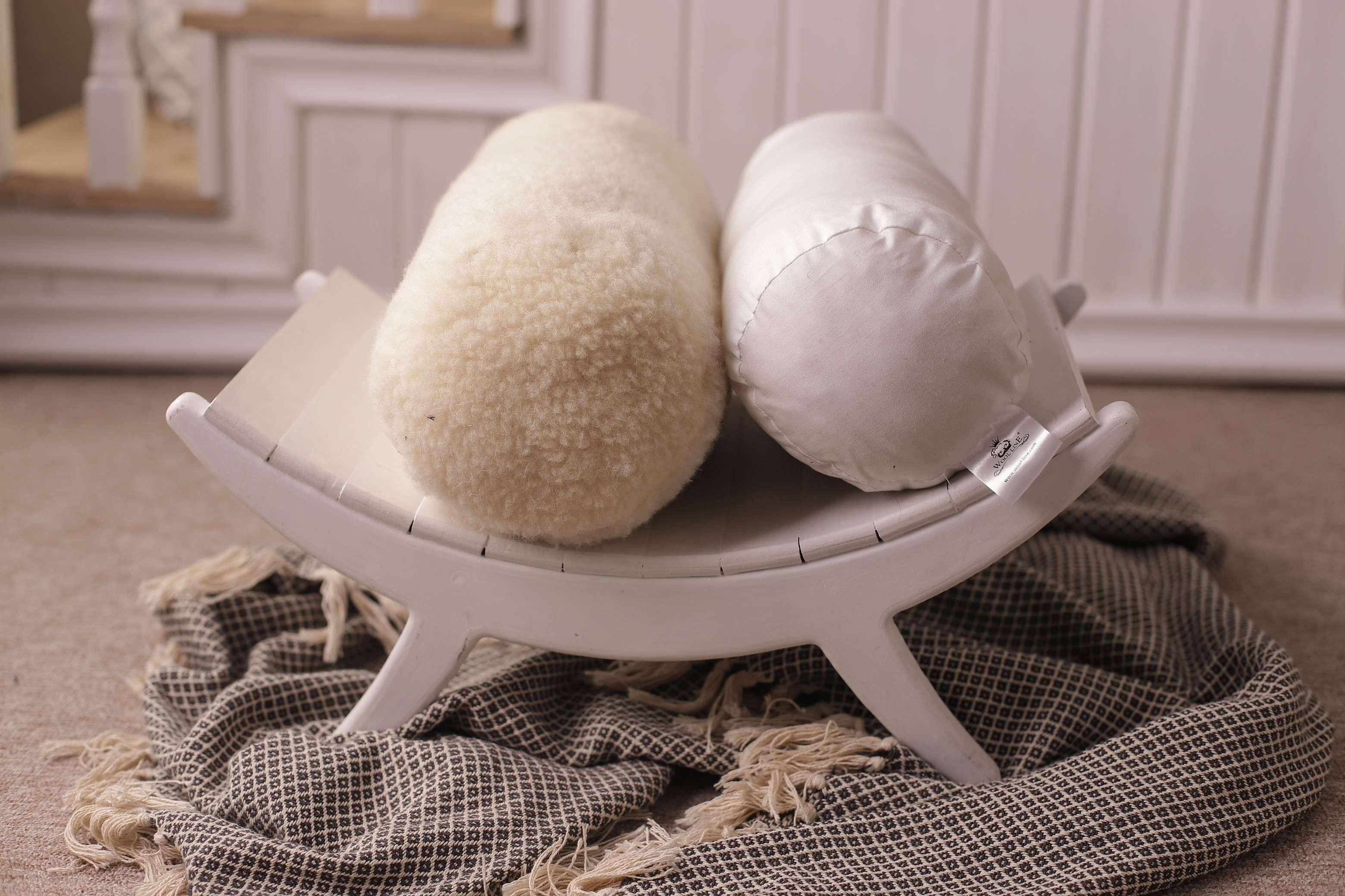 Zwei unserer Nackenrollen nebeneinander auf einer weißen Holzablage abgestellt. Links befindet sich die Nackenrolle Natur mit Filzbezug, rechts ist die Nackenrolle aus Bio-Baumwollbezug zu sehen. 