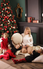 Eine Familie tobt sich aus und hält dabei runde Kissen von Wool-Line in den Händen. Ein kleines Mädchen hält sich unser Rundkissen über den Kopf und ist im Begriff, den Kopf bequem darauf abzulegen. Im Hintergrund befindet sich ein bunt geschmückter Weihnachtsbaum. 