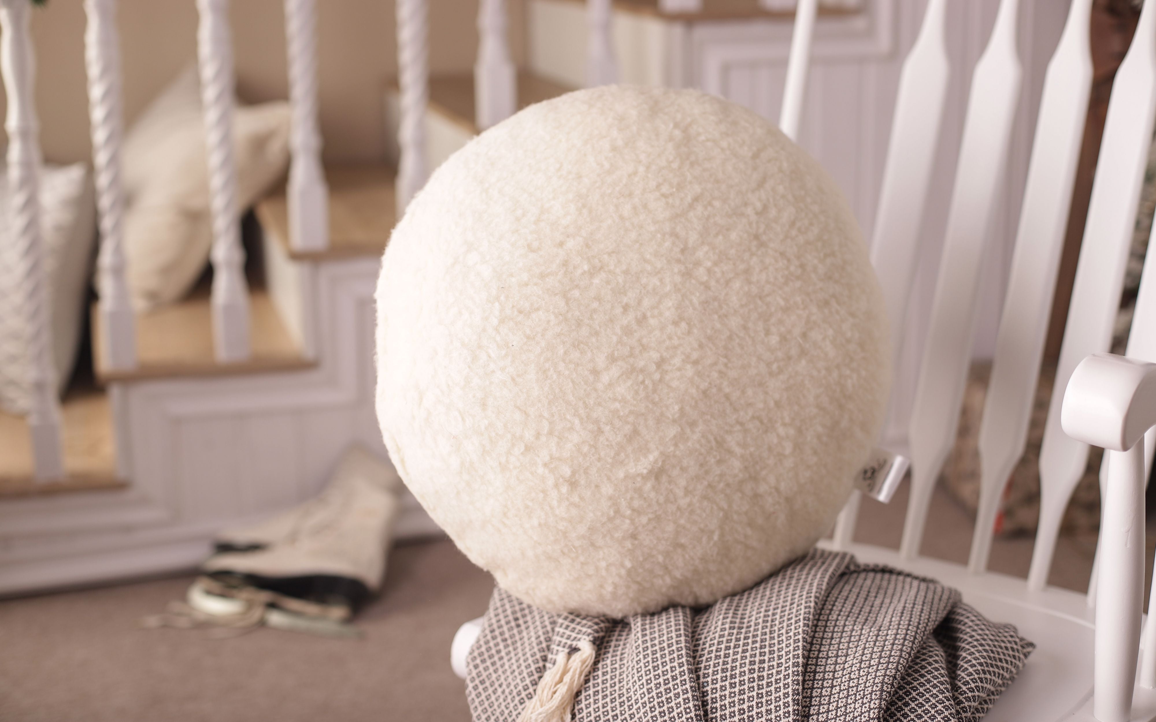 Ein rundes Kissen aus echter Schafschurwolle dekorativ auf einem weißen Schaukelstuhl aufgestellt. 