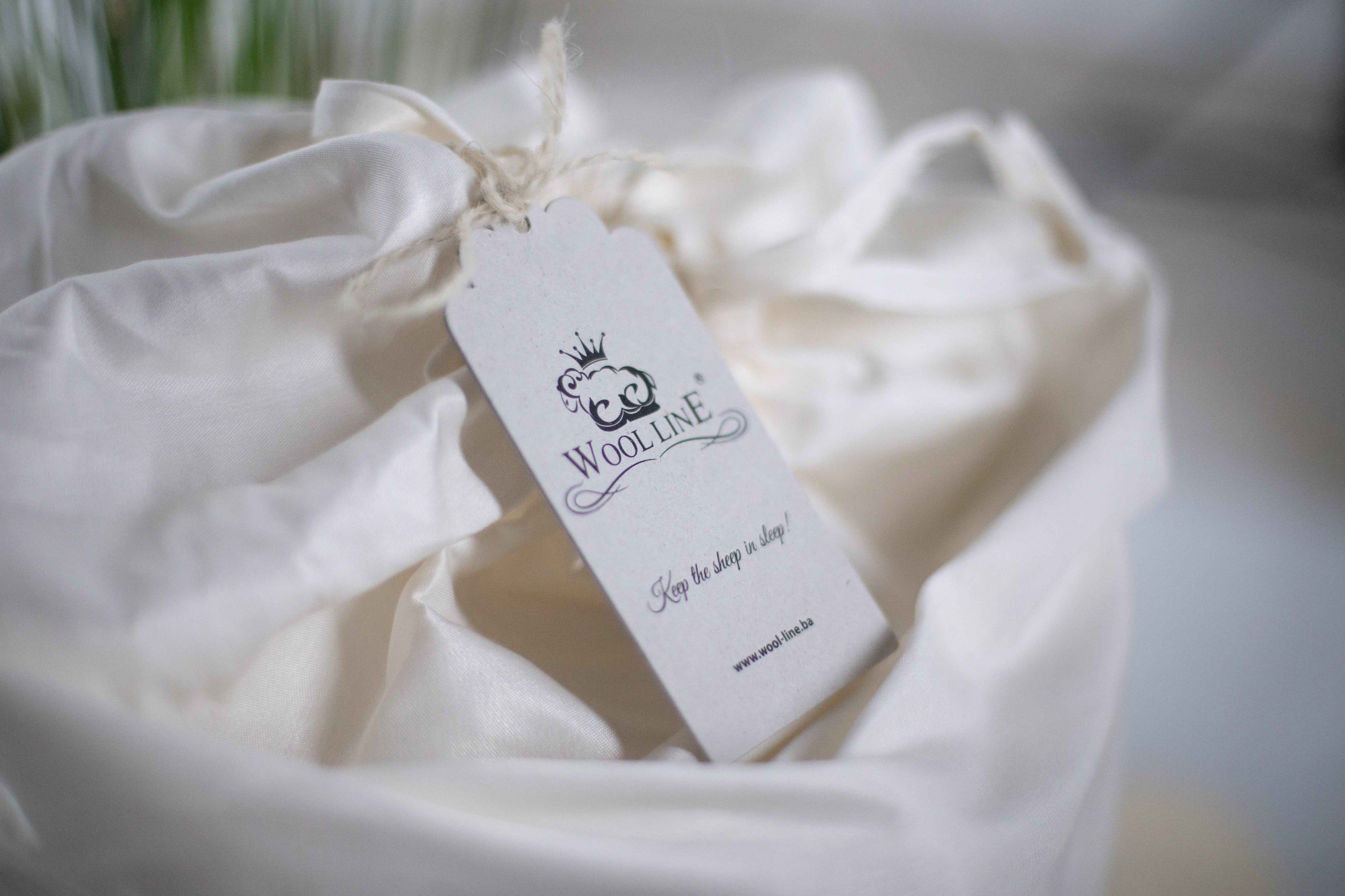 Eine Schafschurwolle Bettdecke Gold befindet sich bereit zum Versand in der Verpackung aus Bio-Baumwolle. In der Mitte befindet sich ein Zettel mit dem Wool-Line Logo. 