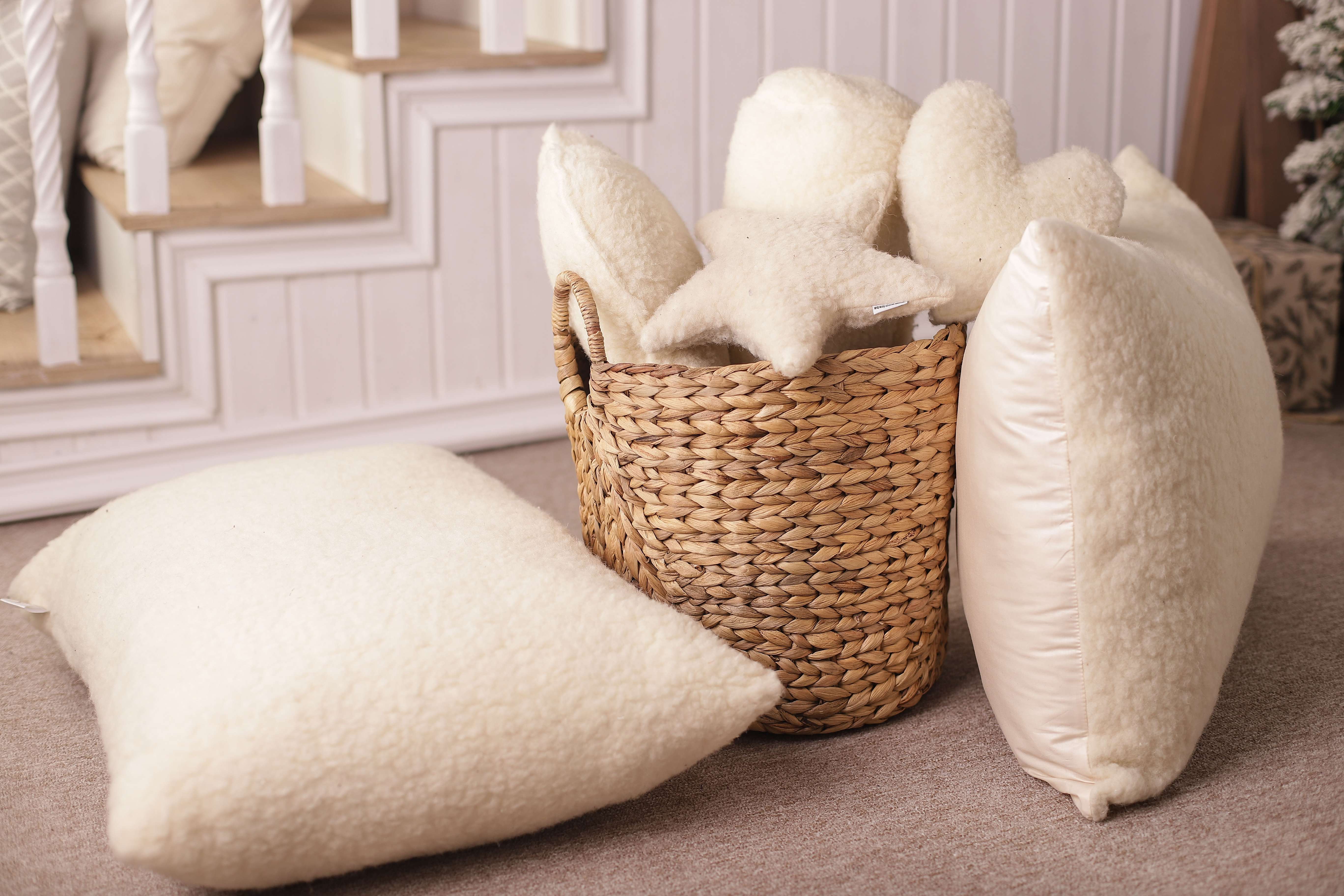 Zwei Schafwolle Kissen Gold/Lux auf dem Boden. Ein Kissen liegt flack neben einem runden Korb, in dem sich vier Dekokissen aus reiner Bio-Schafwolle befinden. Das andere Schafwolle Kissen ist auf der rechten Seite an den Korb angelehnt. 