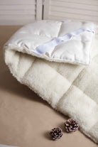 Der Topper aus 100% biologischen Materialien von Wool-Line liegt halb zusammengefaltet auf dem Untergrund. Im Vordergrund verstärken zwei Tannenzapfen die Szenerie. 